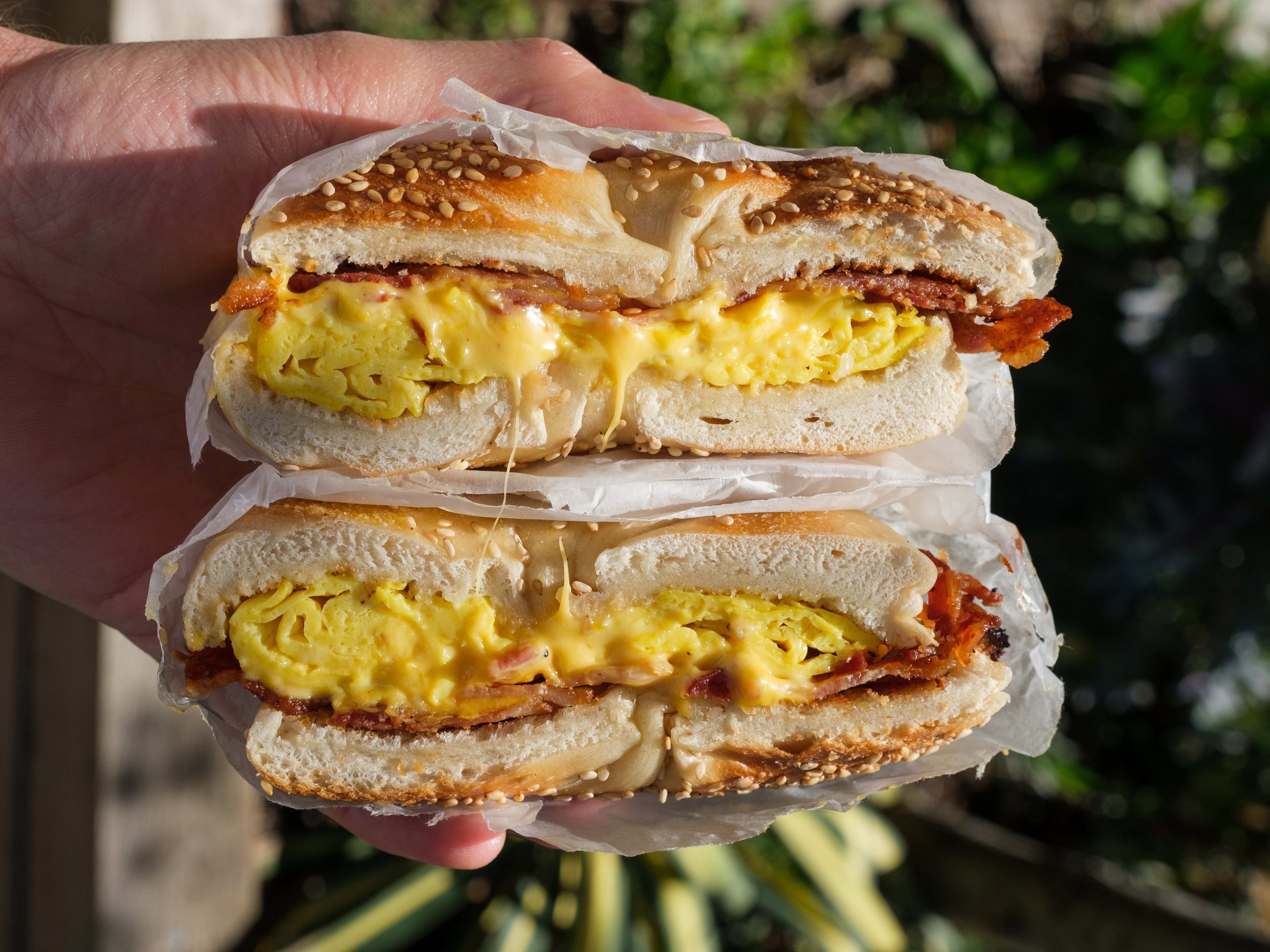 A bacon egg and cheese sesame bagel held with both halves stacked.