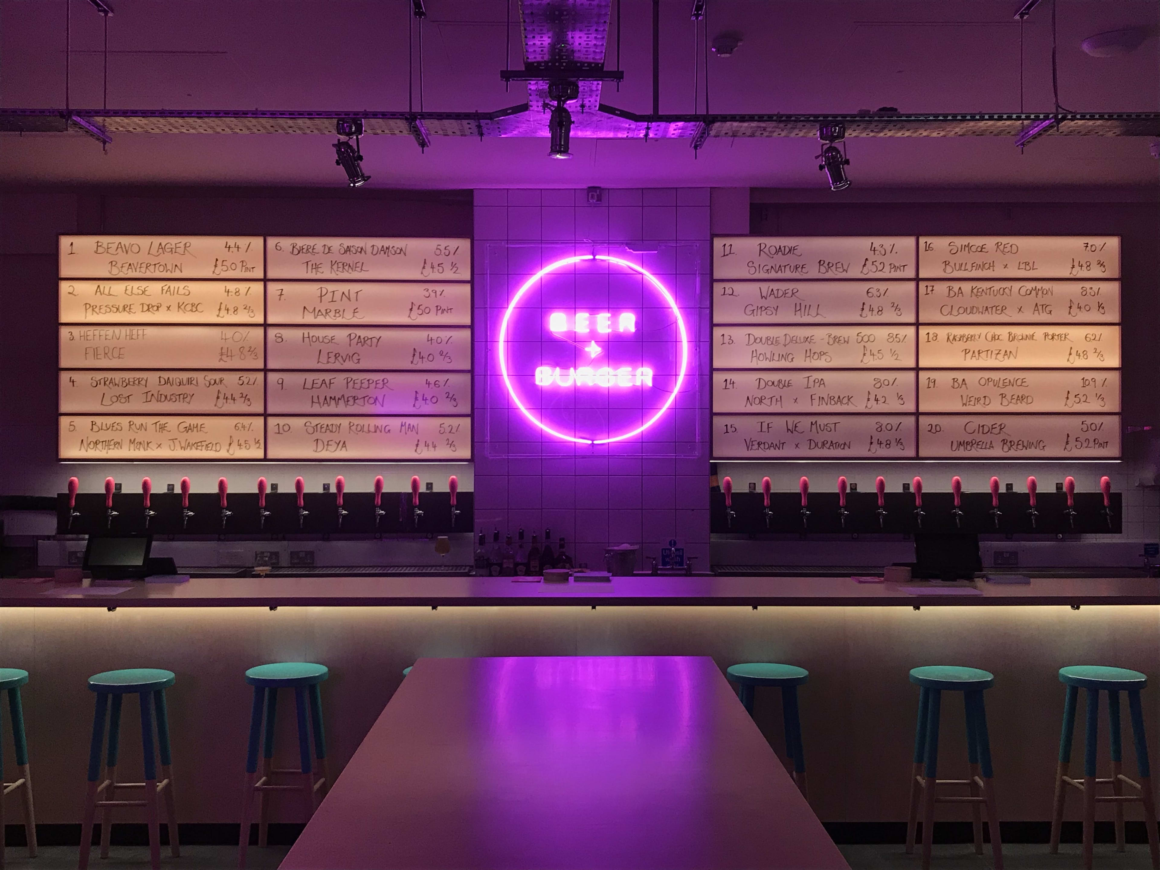 The bar at Beer + Burger. A neon purple sign is in the center of the wall.