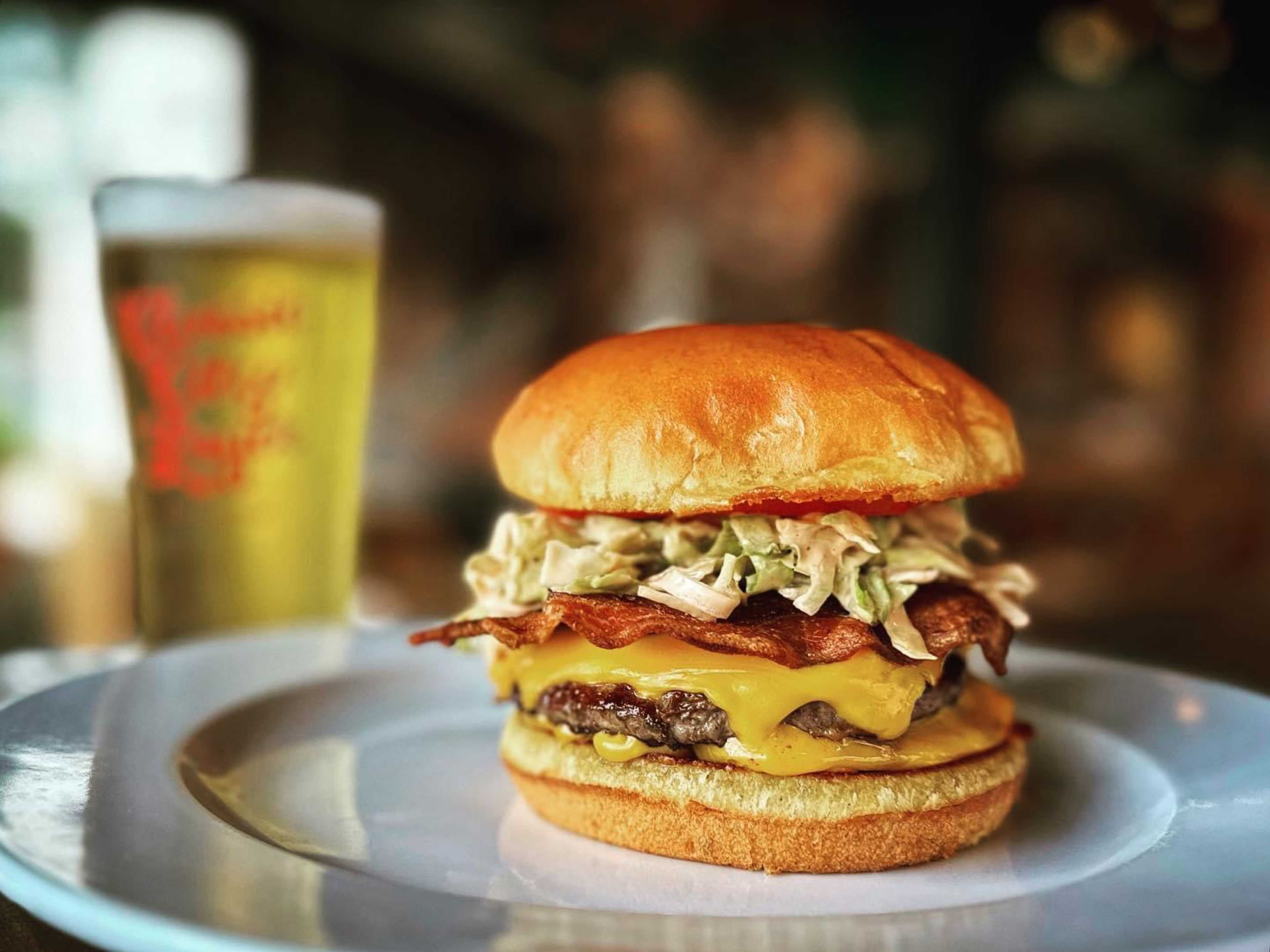 Burger with Million dressing, backon and cheese on a white plate with a beer in the background.