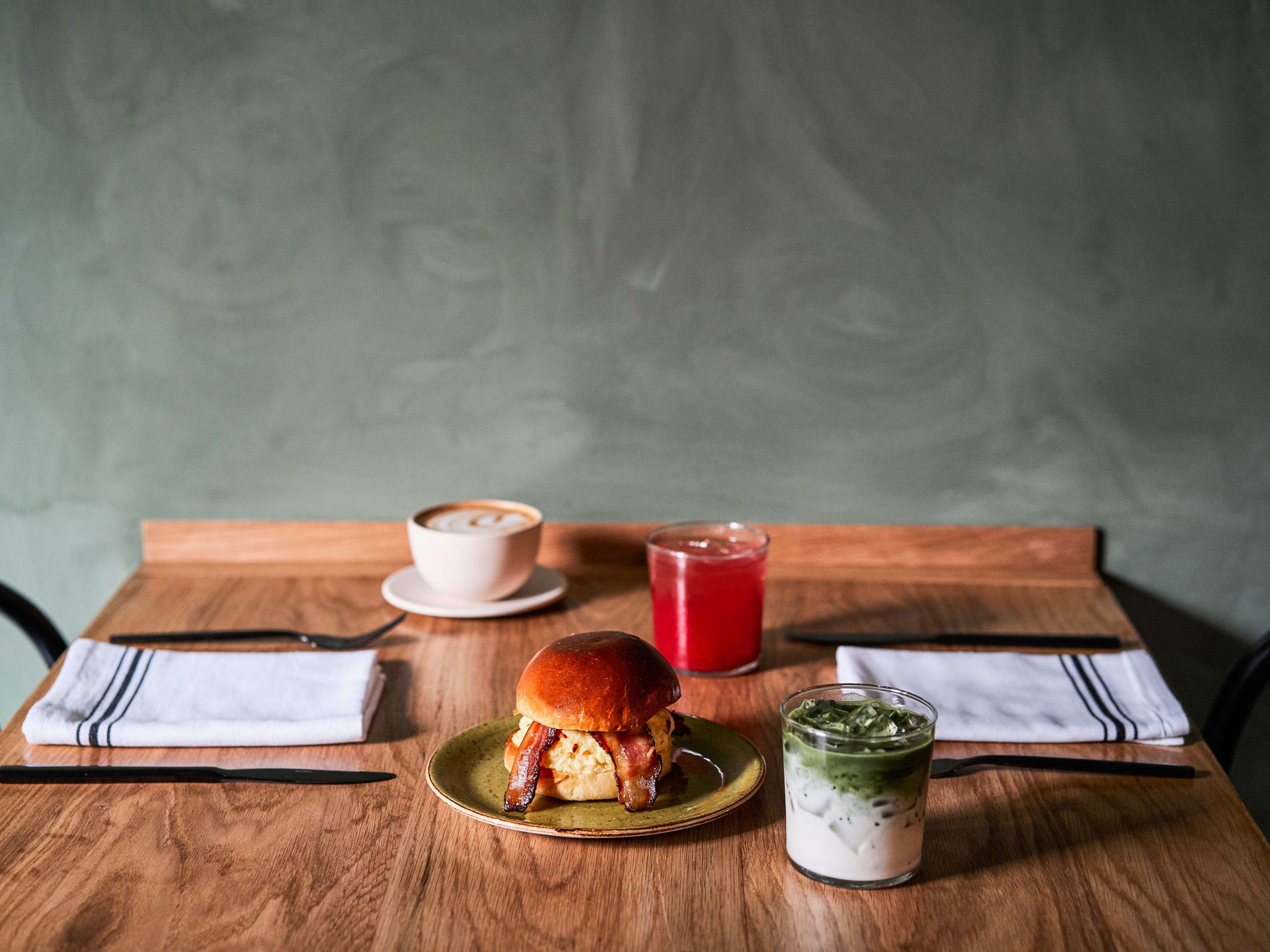 A breakfast sandwich on a table beside an iced matcha.