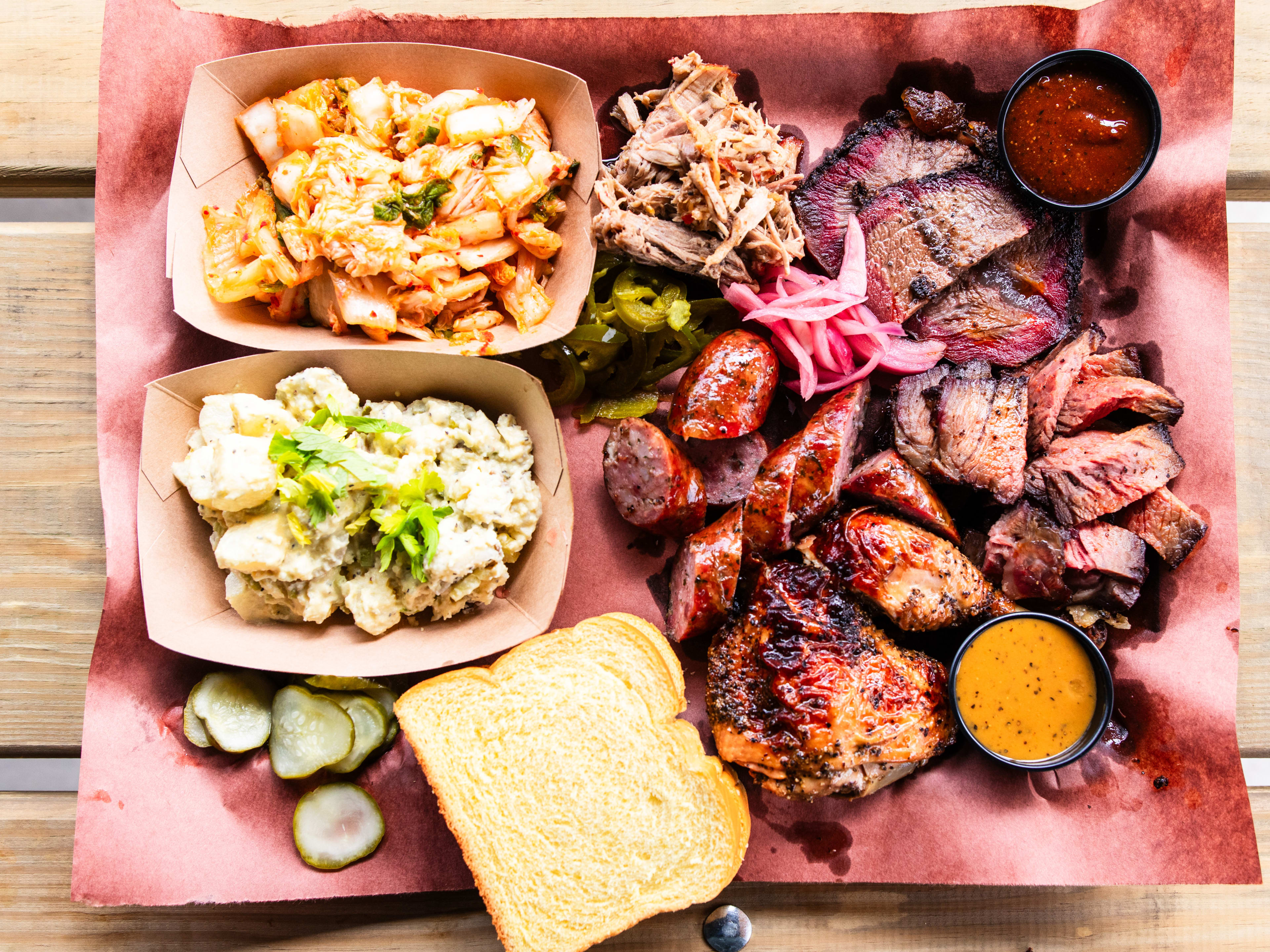 A tray of mixed barbecue, sides and bread served on butcher paper.