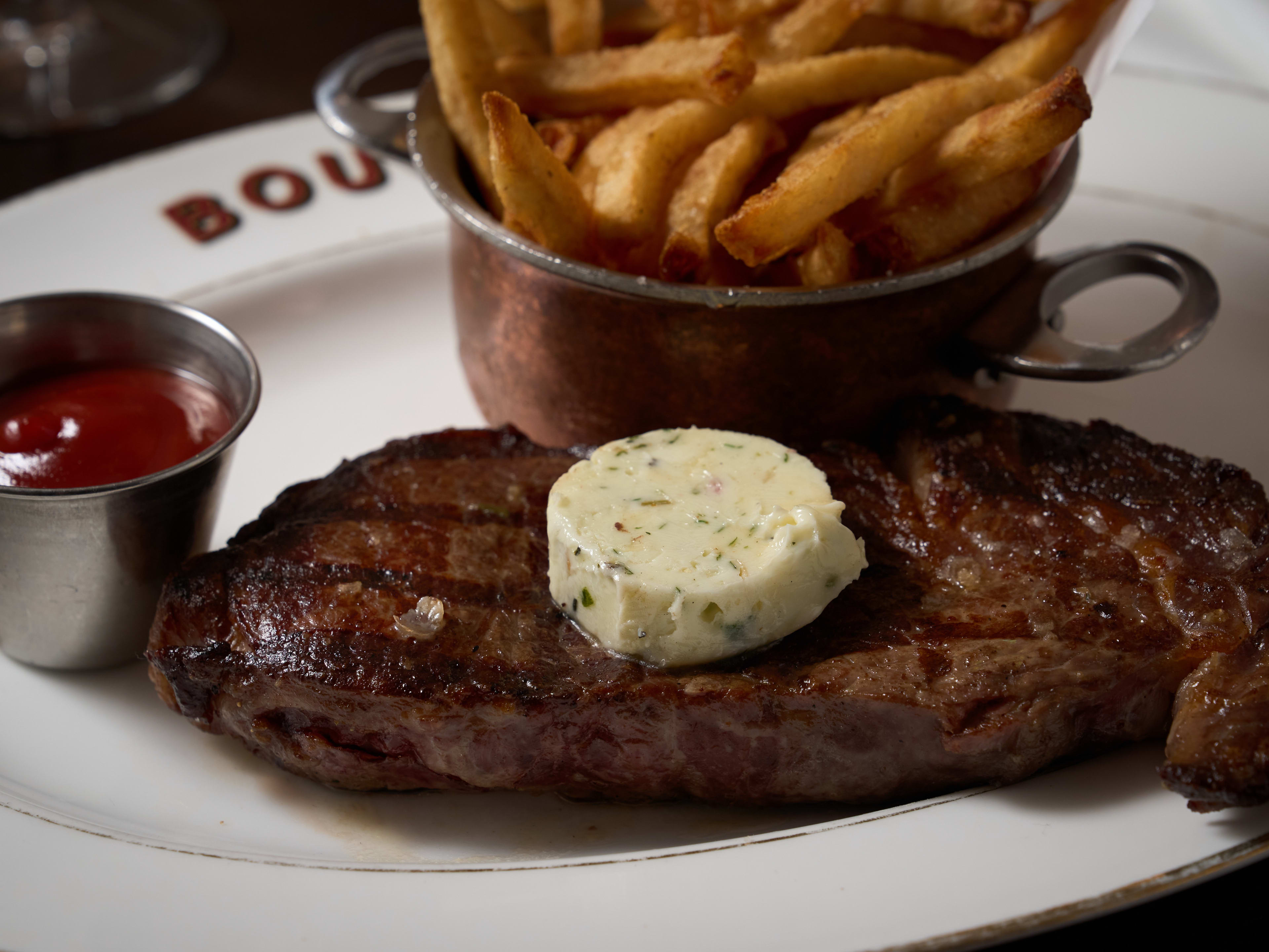 Plate of steak topped with a compound butter and a side of ketchup and frites