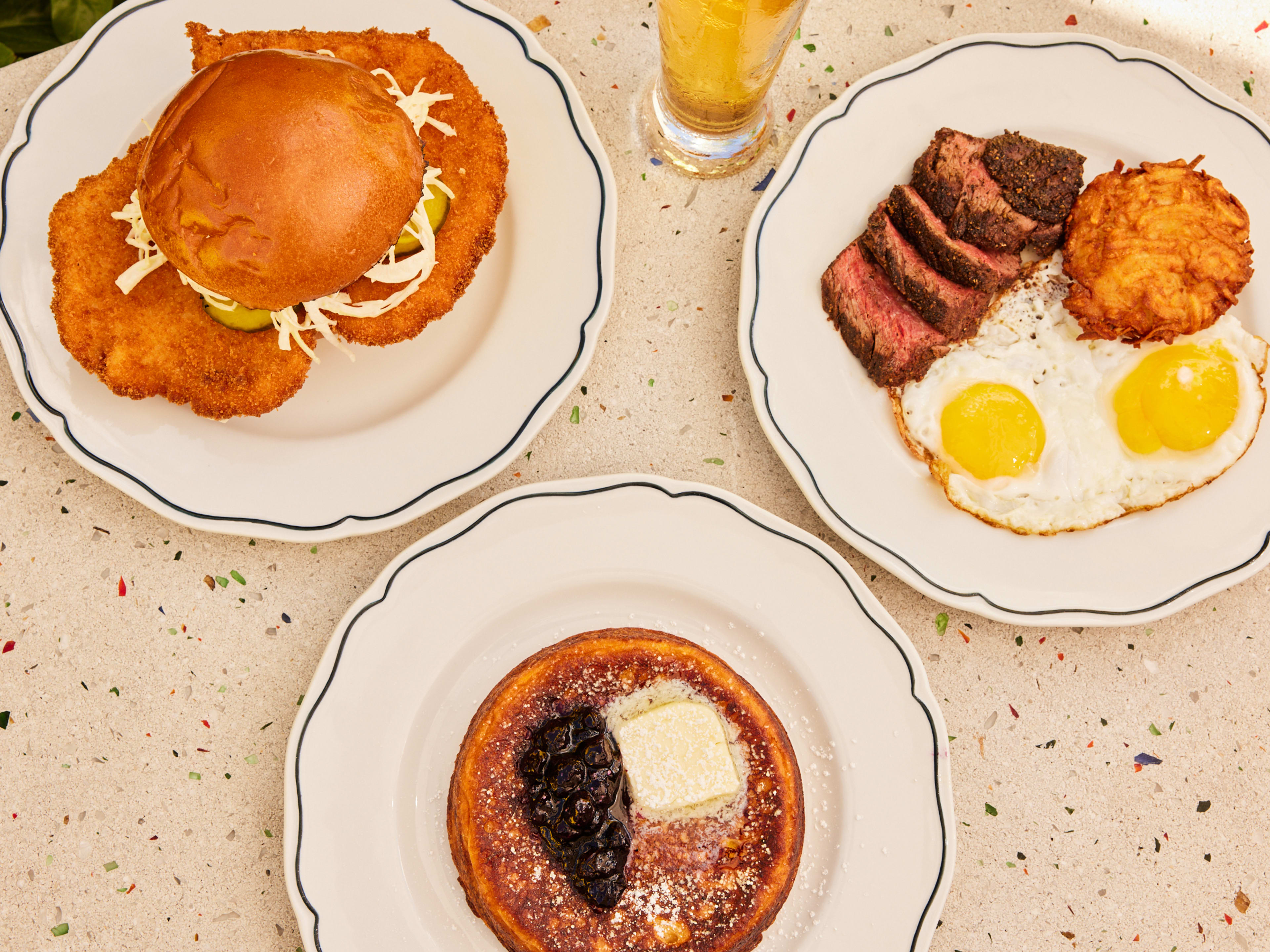 A sandwich, steak and eggs, and a pancake on a table.