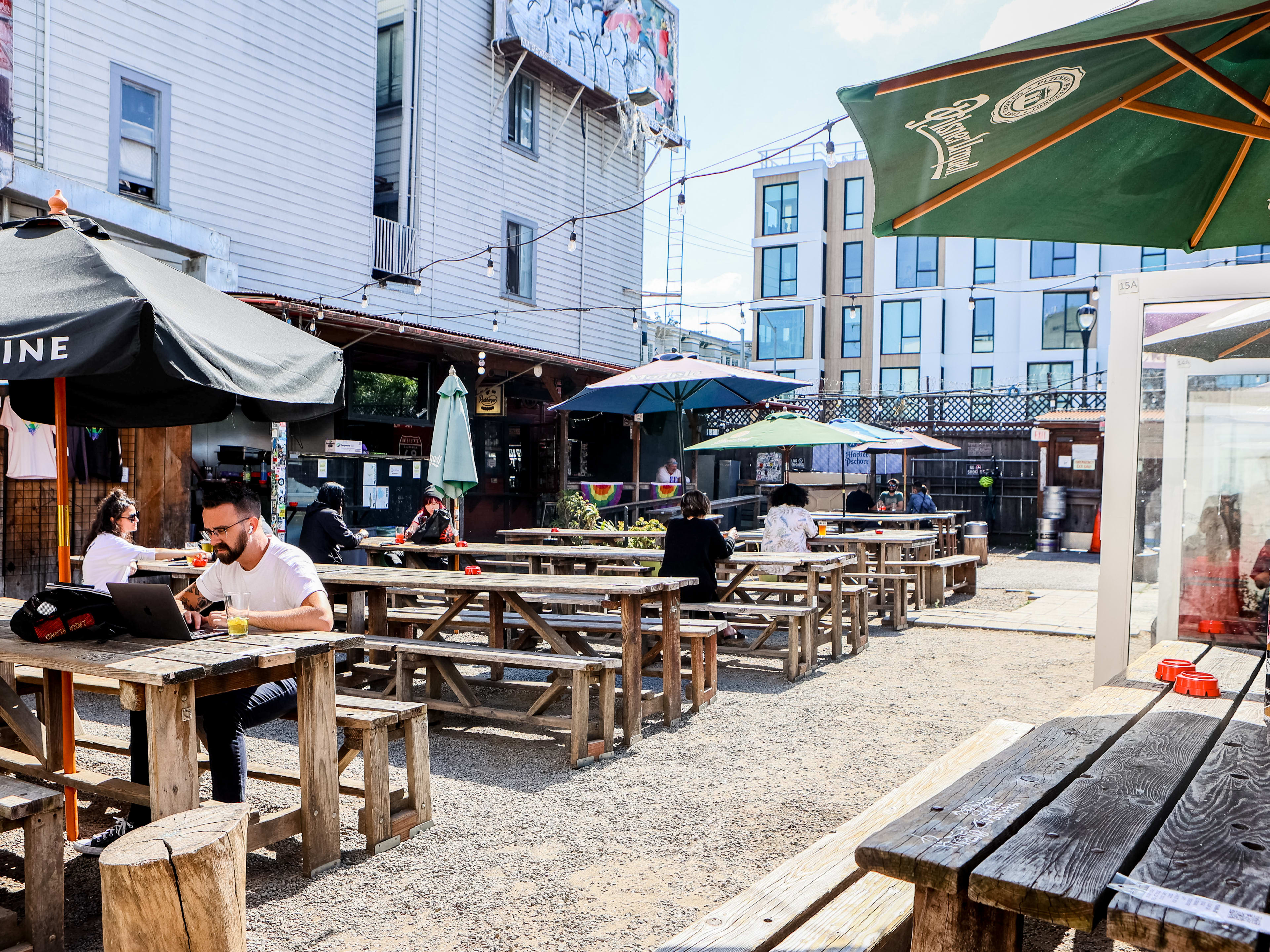 Sunny outdoor bar patio with umbrellas and long wooden tables.