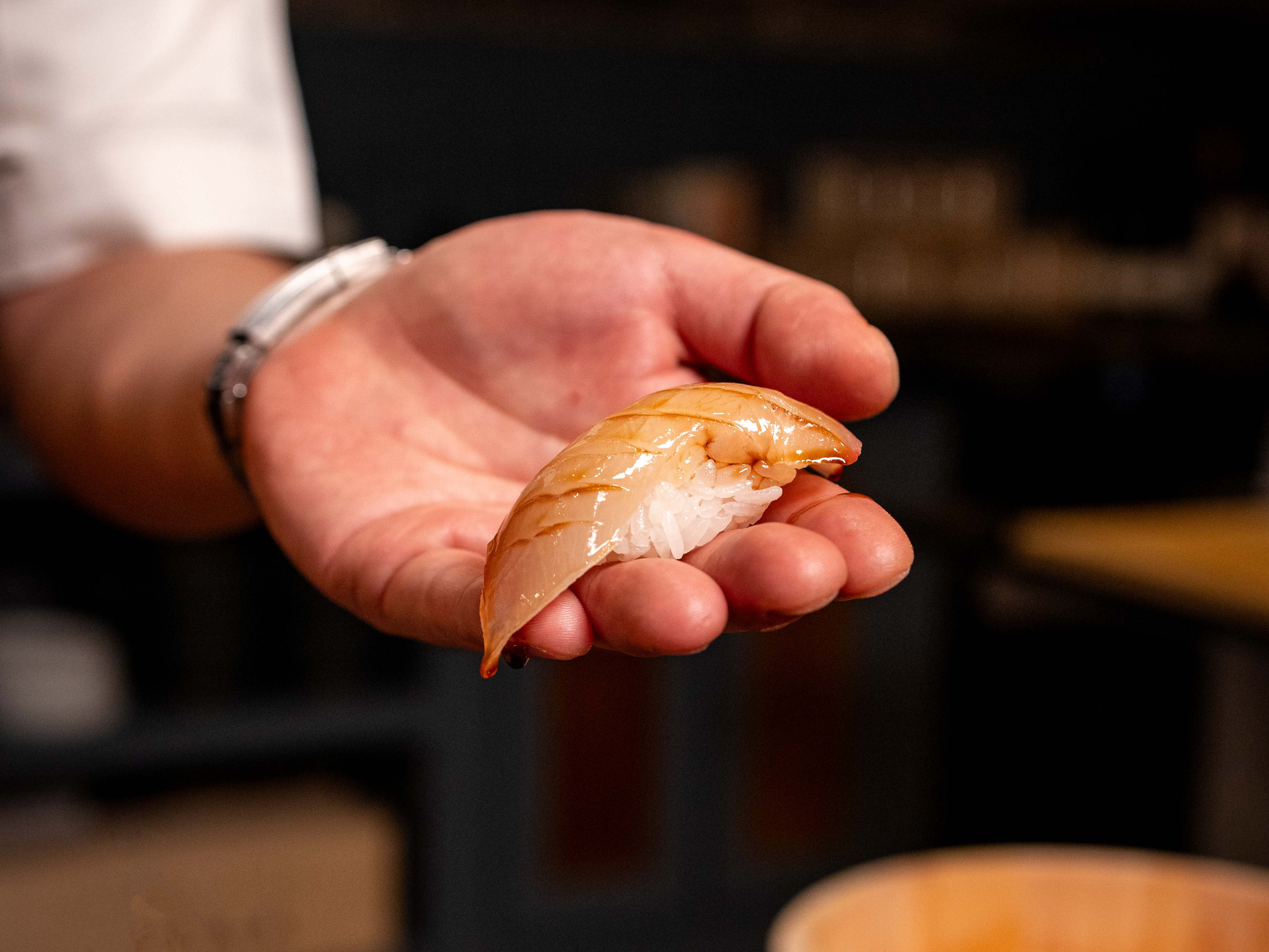 A sushi chef holds a piece of nigiri from Craft Omakase in their hand.