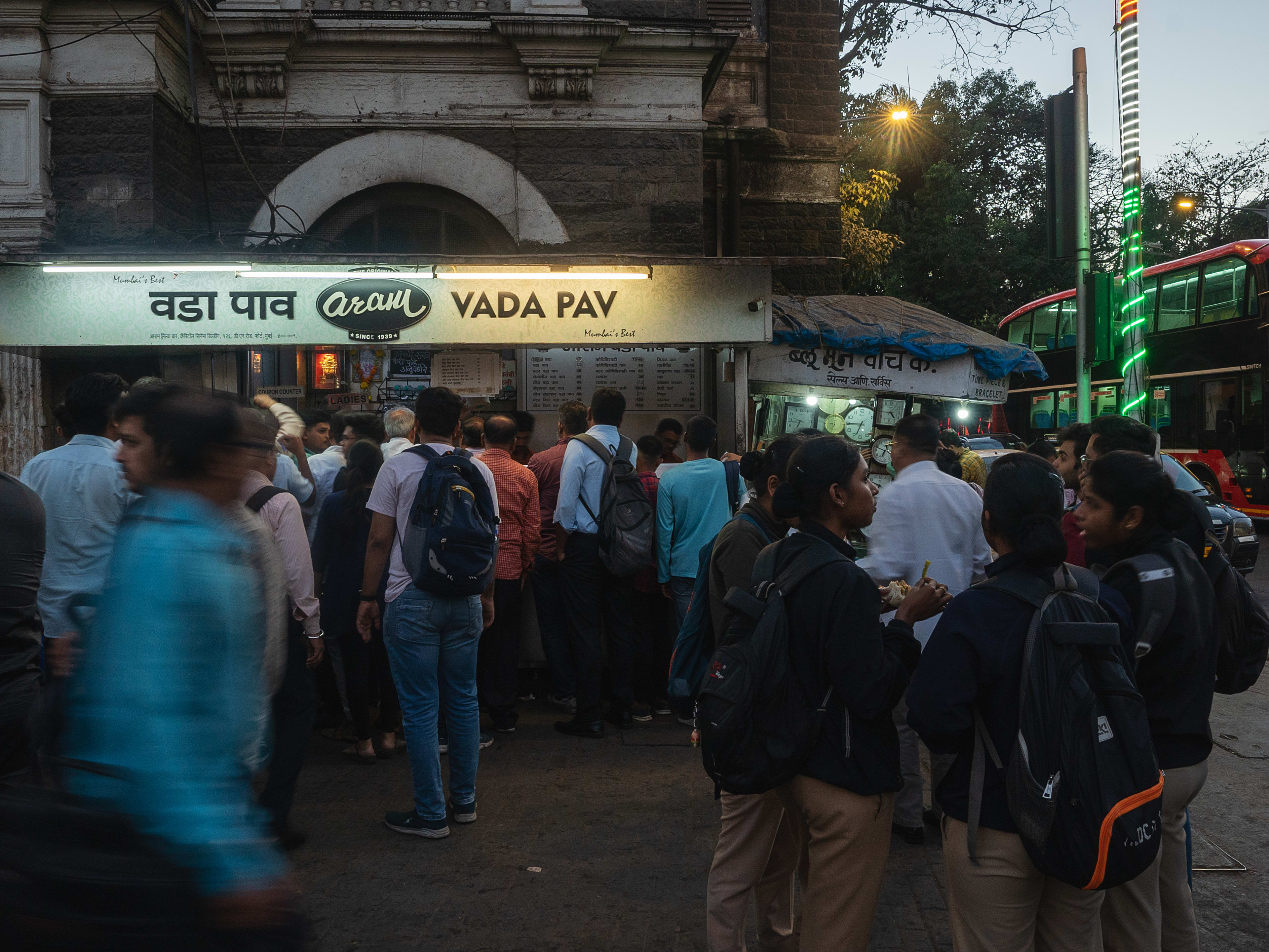 Bustling exterior of Adam Vada Pav at dusk