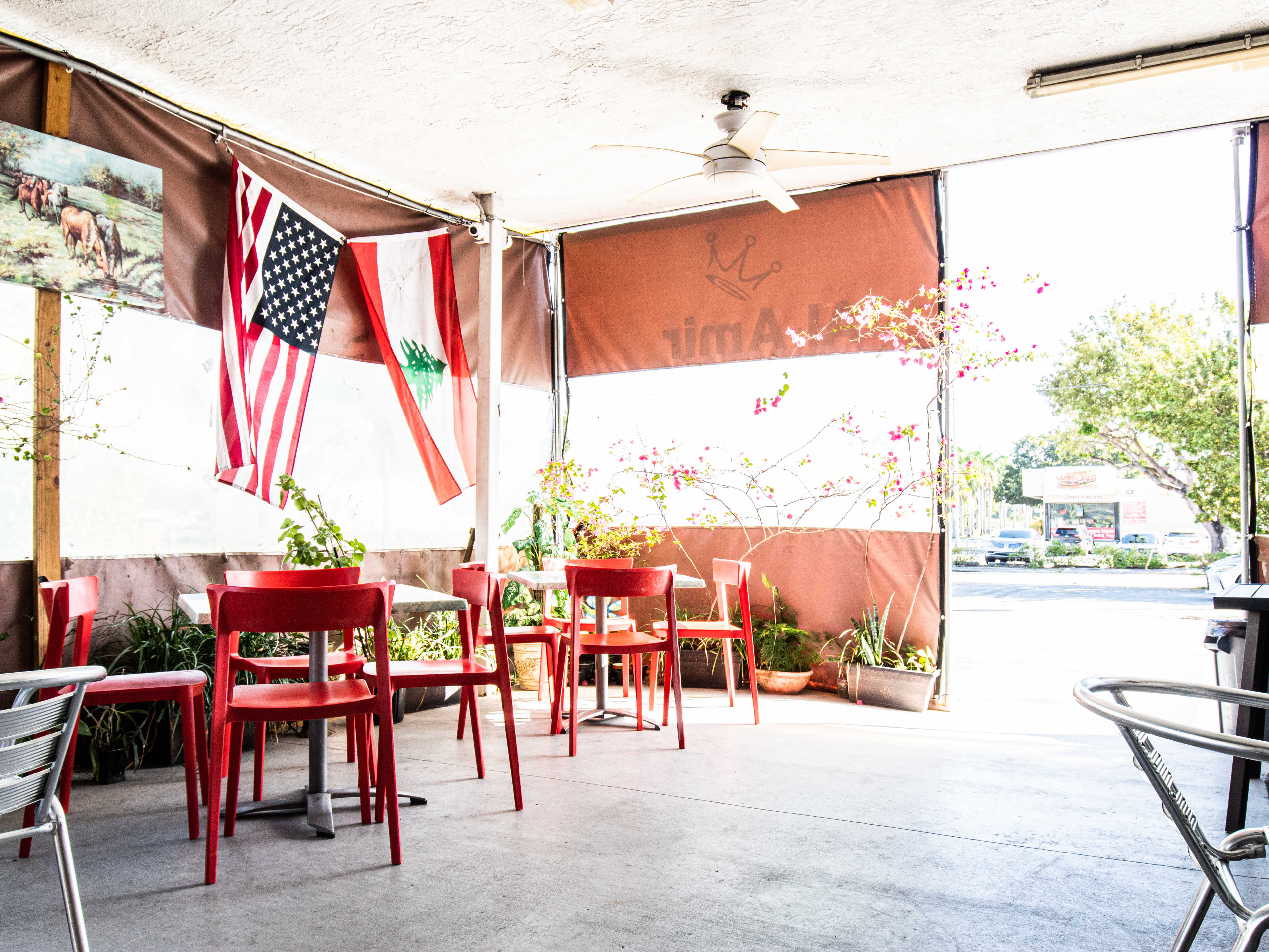 covered outdoor tent patio with flags, tables, and chairs, looking out onto tree-lined street