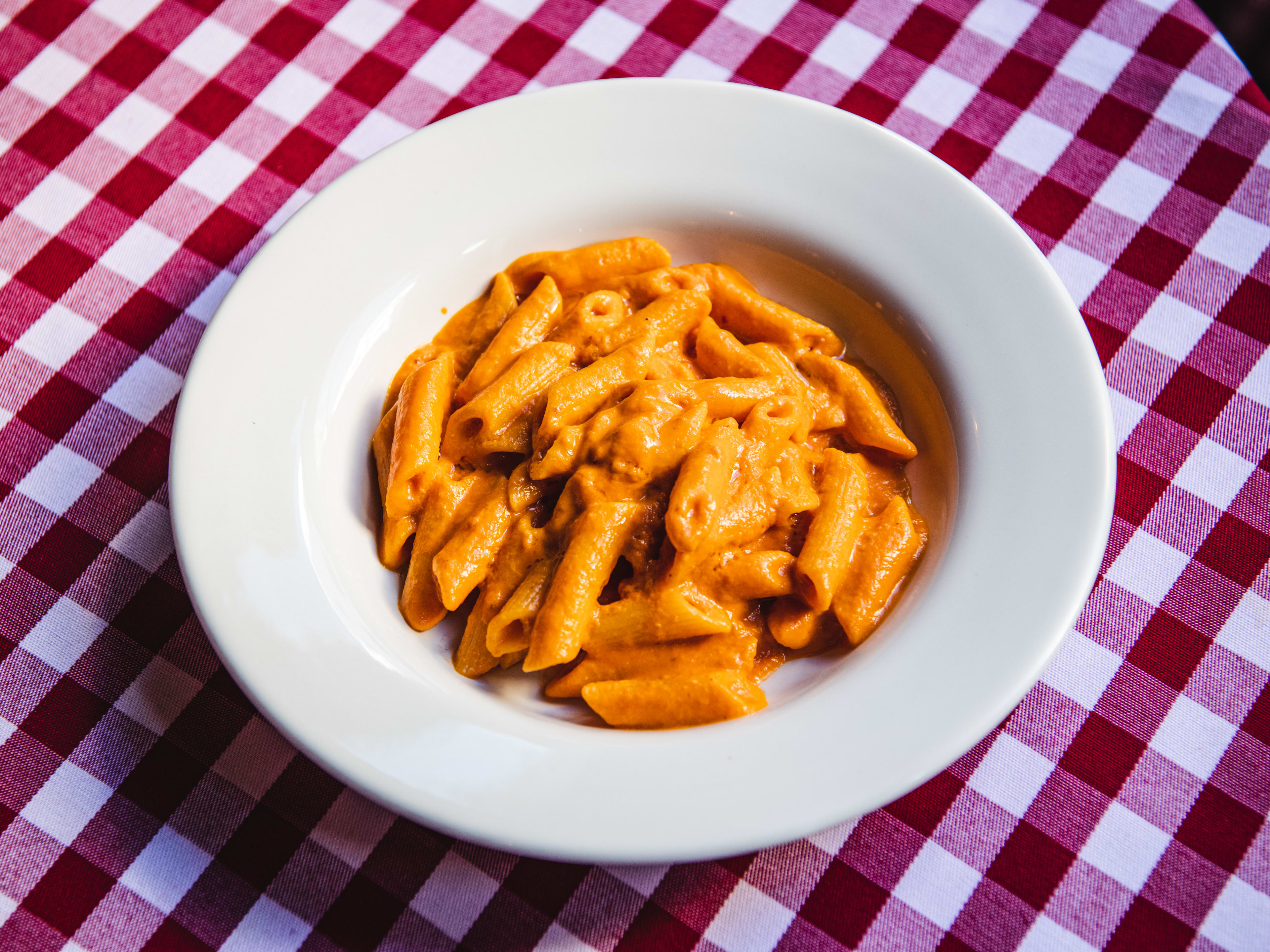 A bowl of penne tomato vodka on a gingham tablecloth.