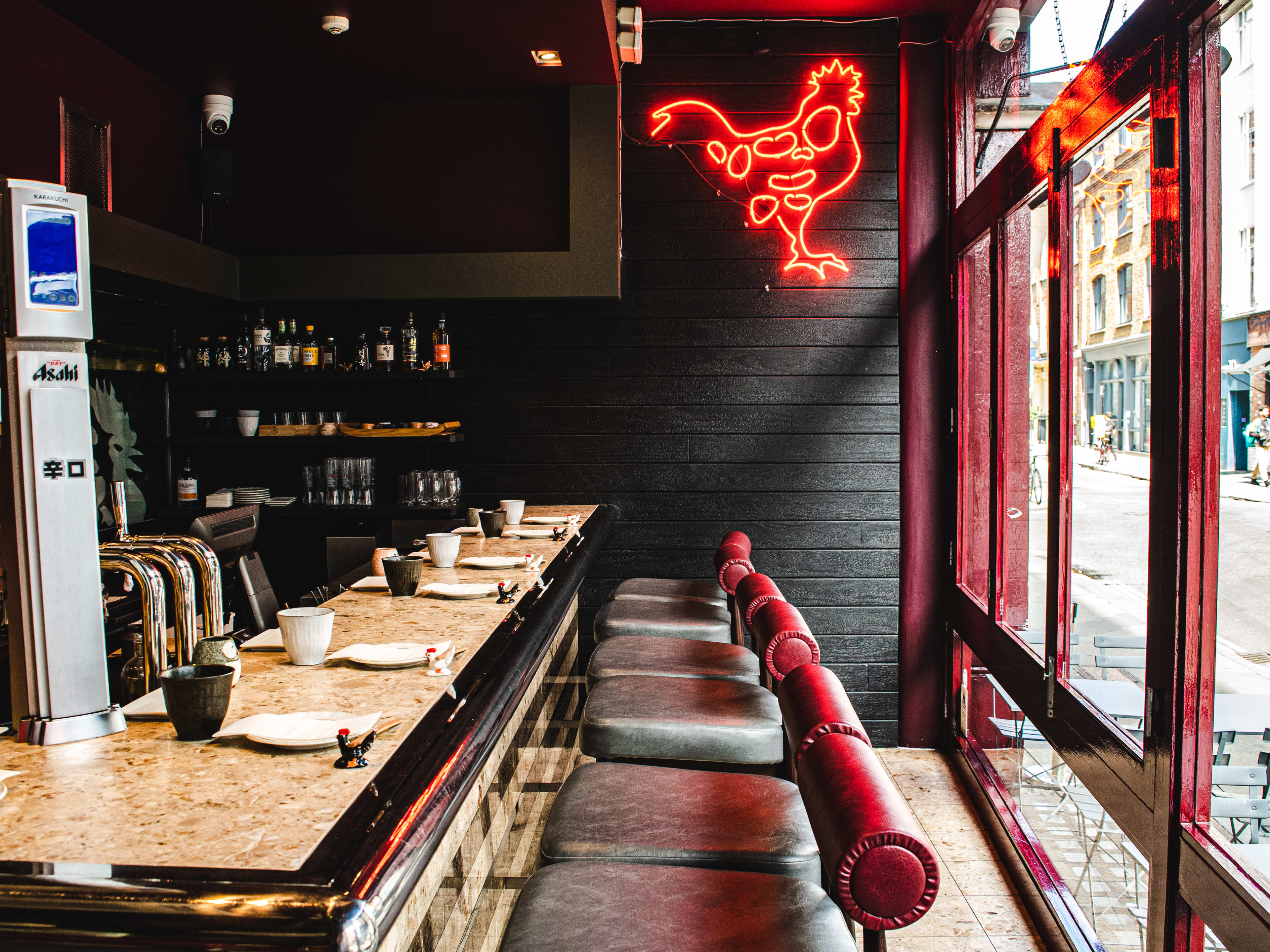 The interior of Humble Chicken with a small a bar with leather bar stools and a neon chicken sign on the wall.