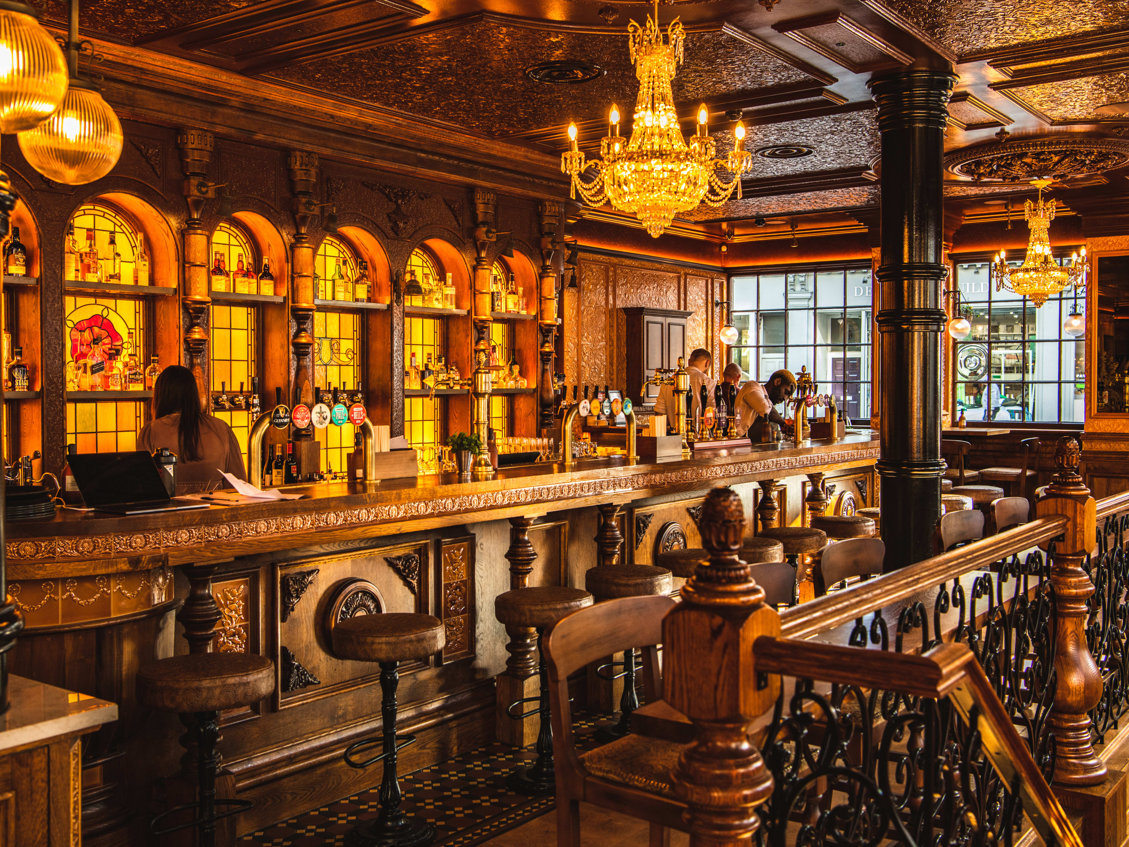 The ornate wooden bar at The Cadogan Arms. There a stained glass windows and chandeliers.