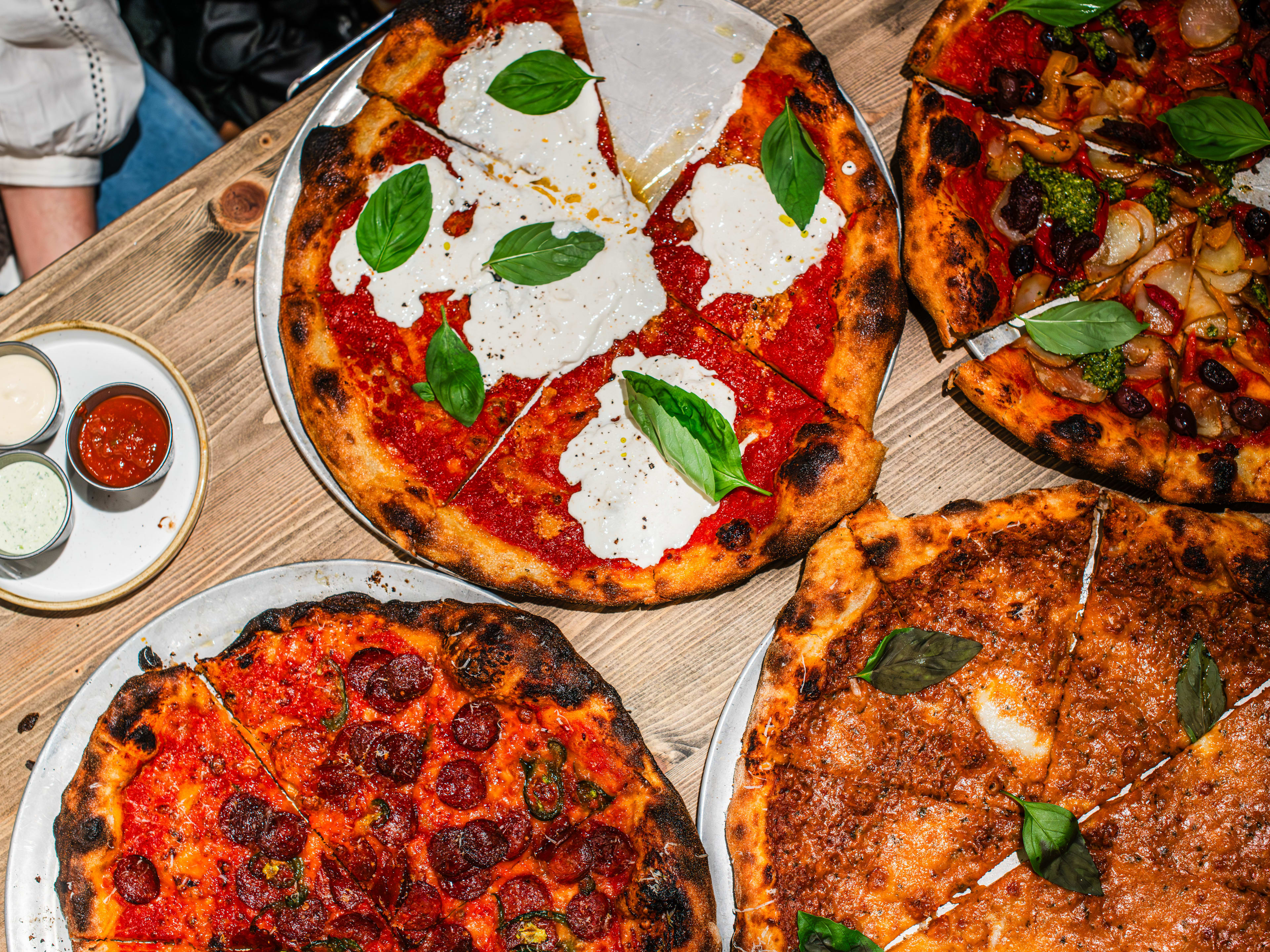 A variety of pizzas from Alley Cats Pizza served on metal trays with a side plate of dipping sauces.