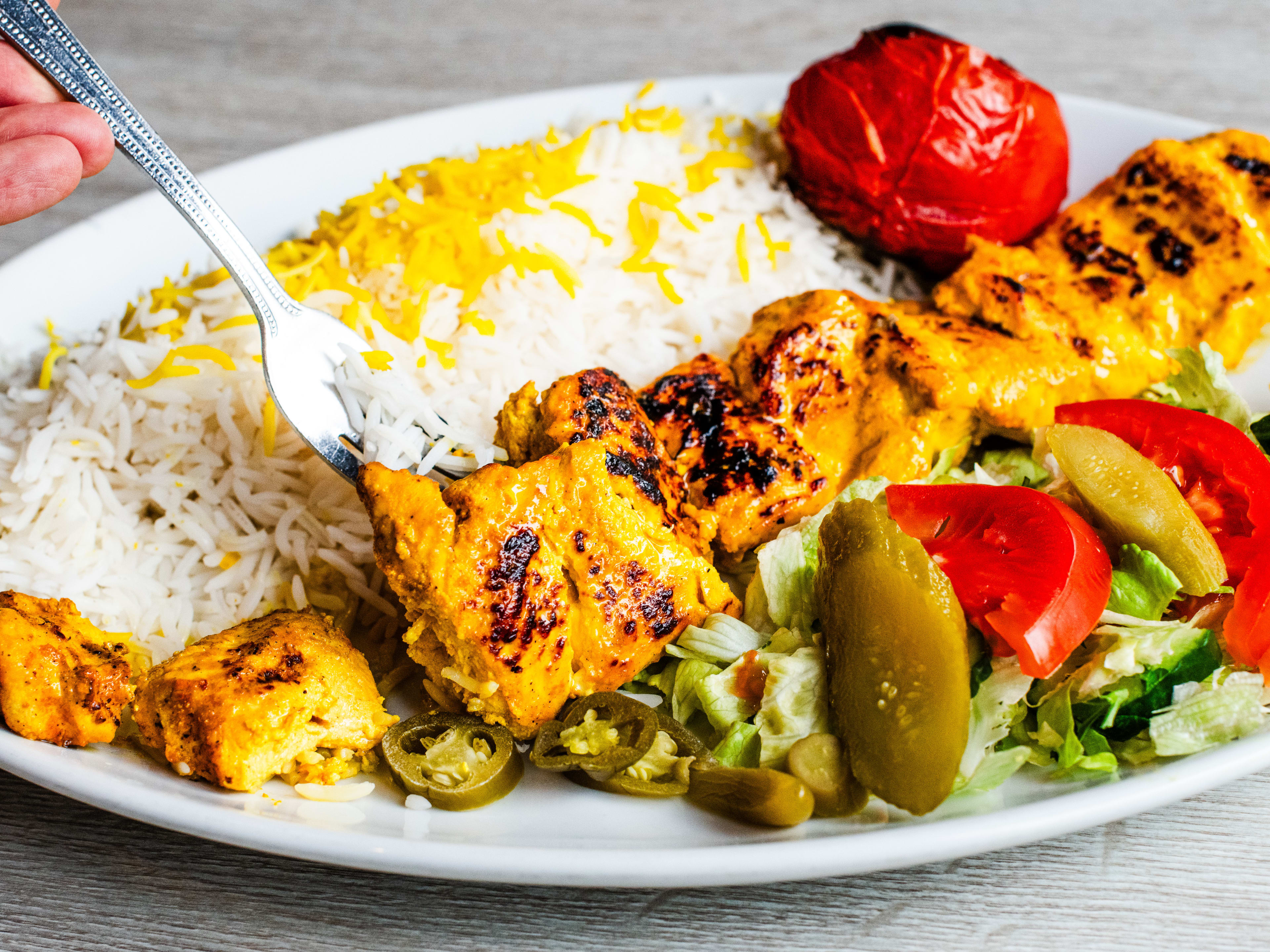 A fork digs into a plate of boneless joojeh with rice.