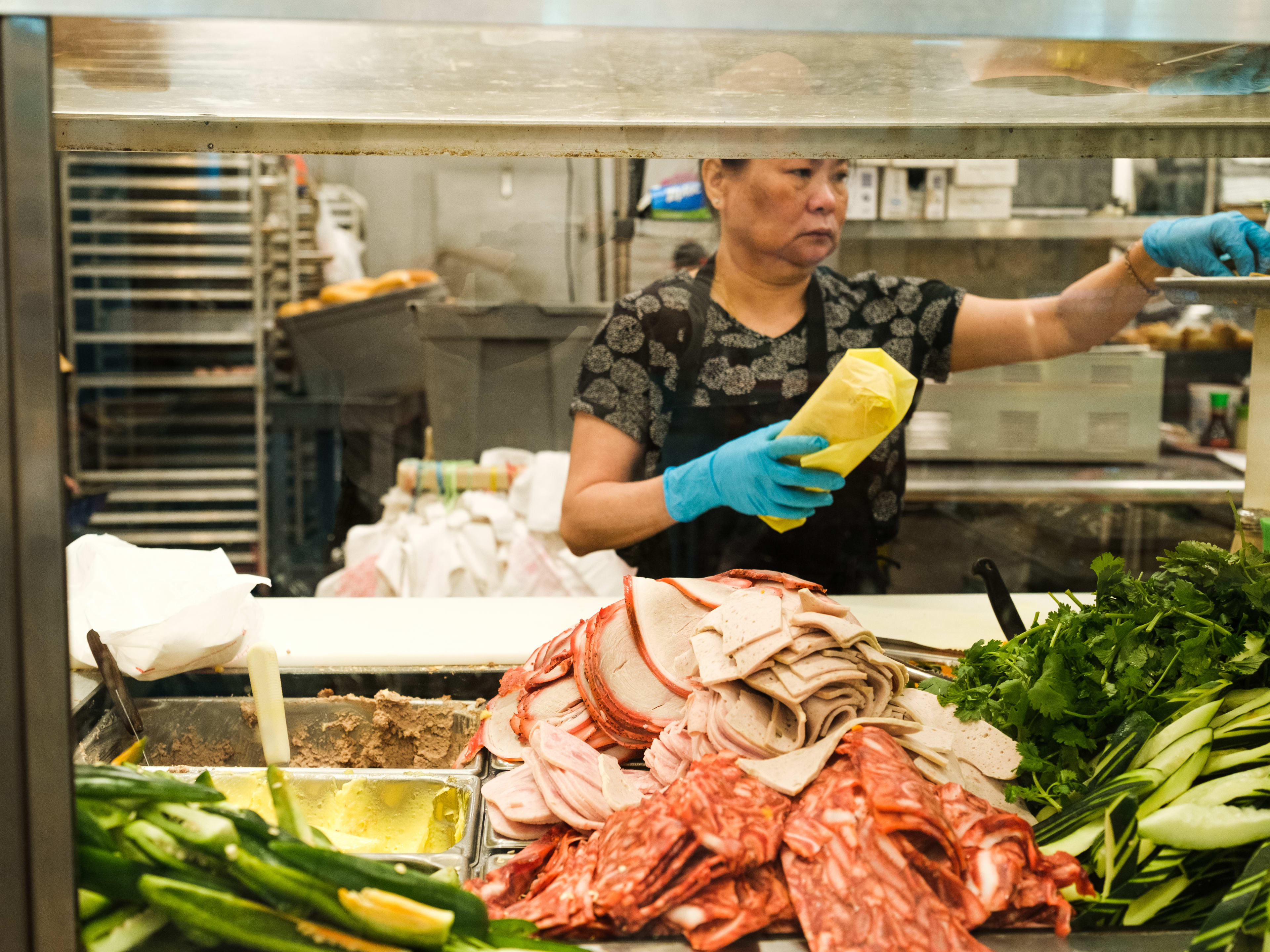 A person making Banh Mi in the kitchen at Alpha Bakery & Cafe.