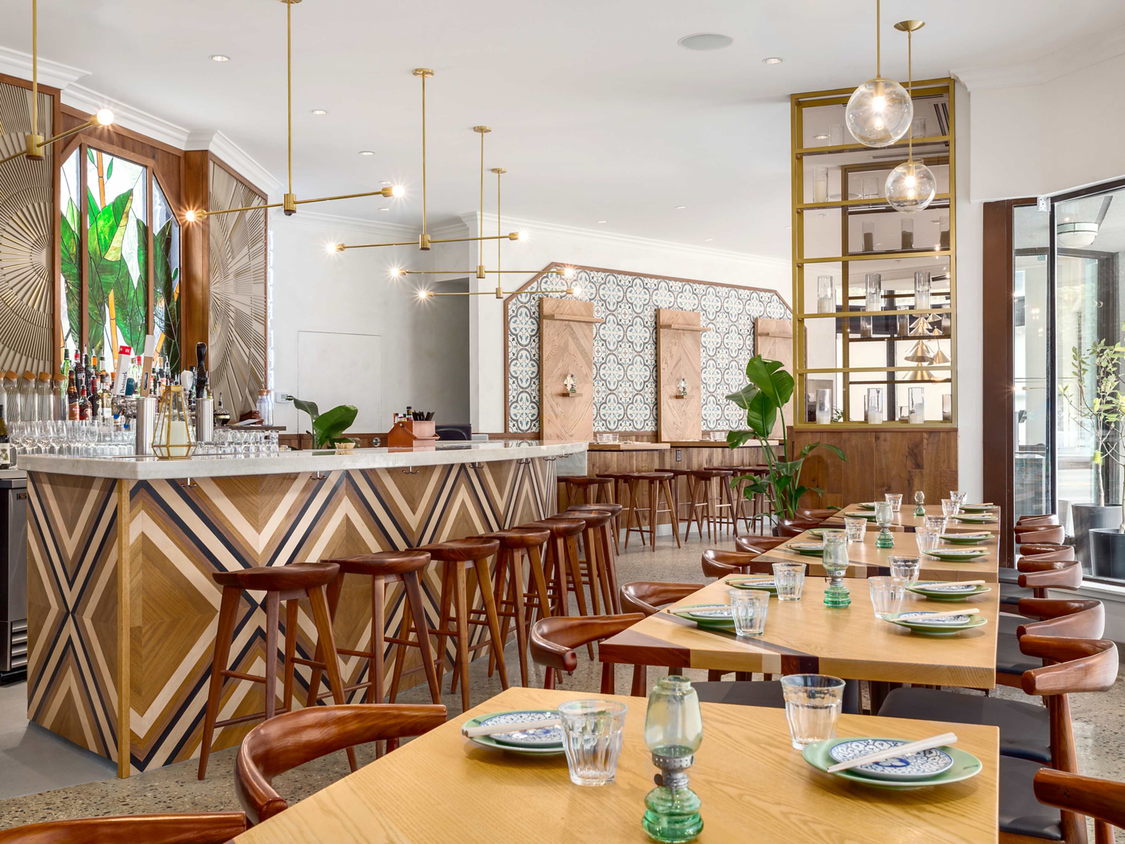 The interior of a casual restaurant during the day, with wooden tables and hanging pendant lights