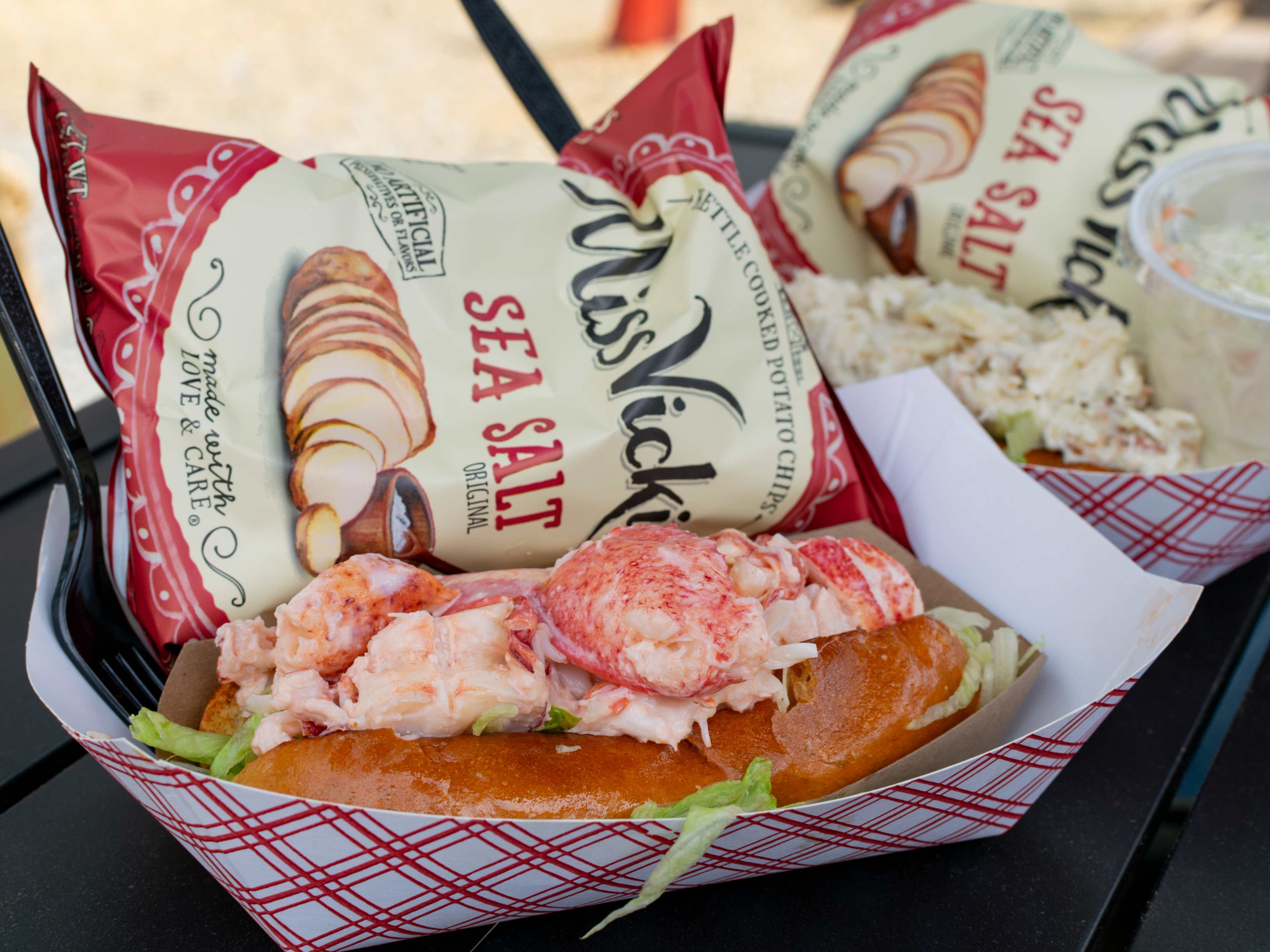 A lobster roll in a paper boat with a bag of potato chips.