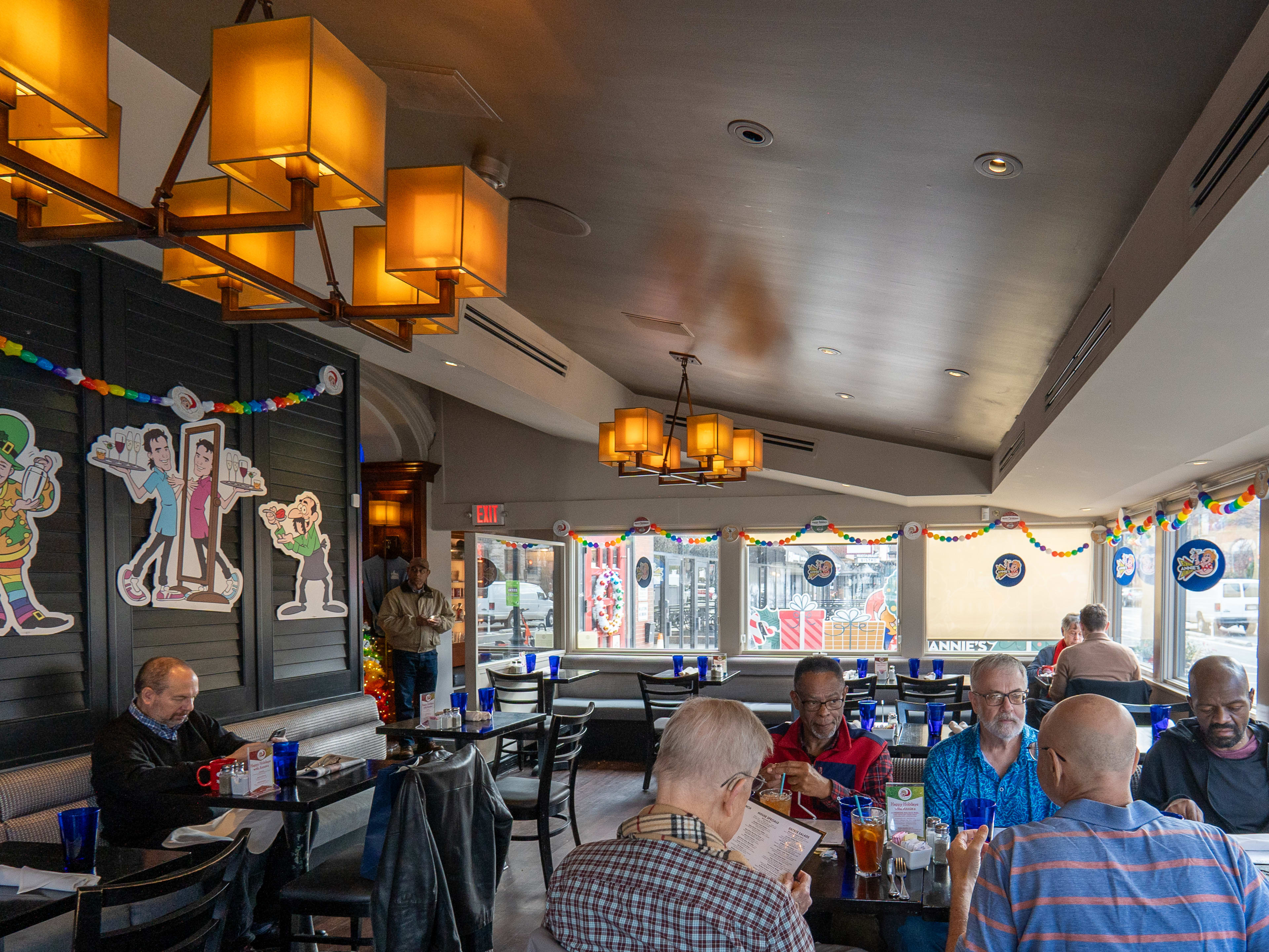 Restaurant interior with modern chandeliers, booths and tables, and a table of men reading the menu.