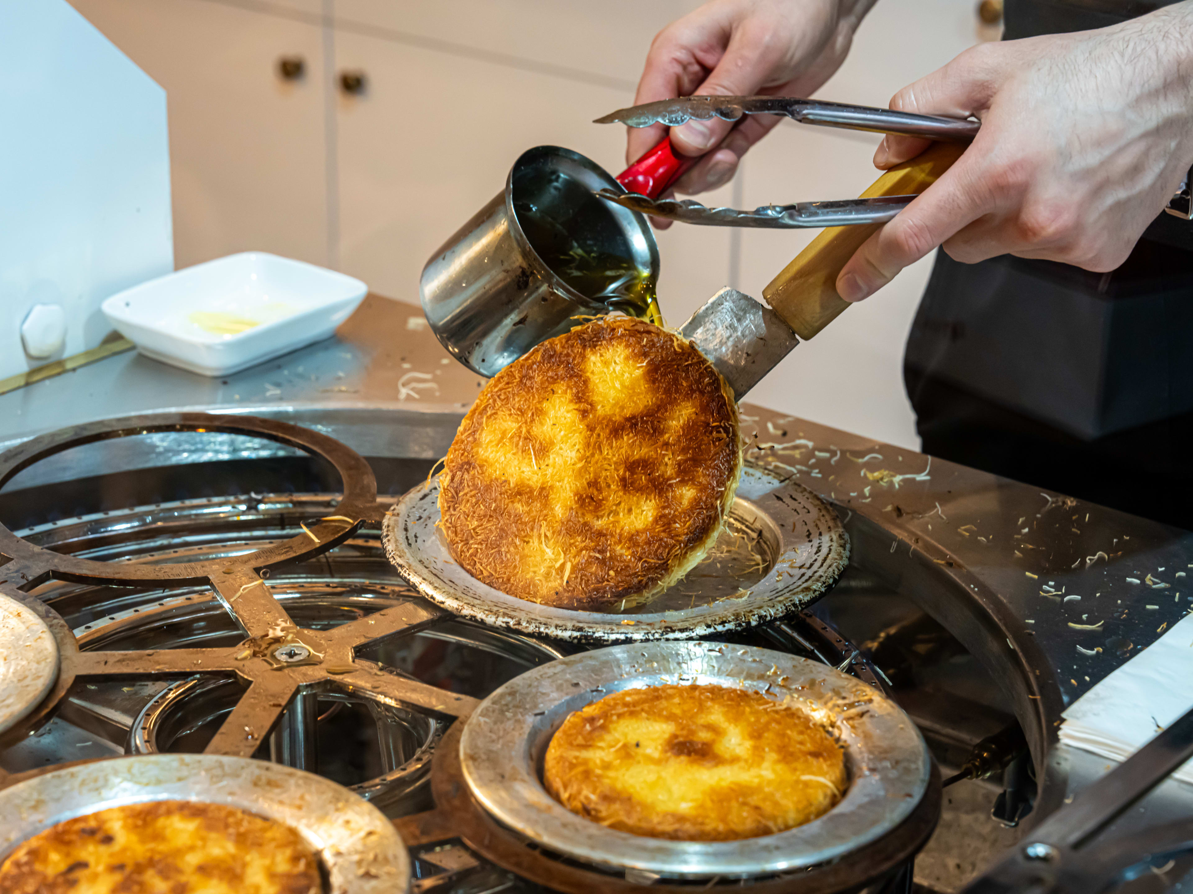 Kunefe being flipped in a pan and syrup being poured on.