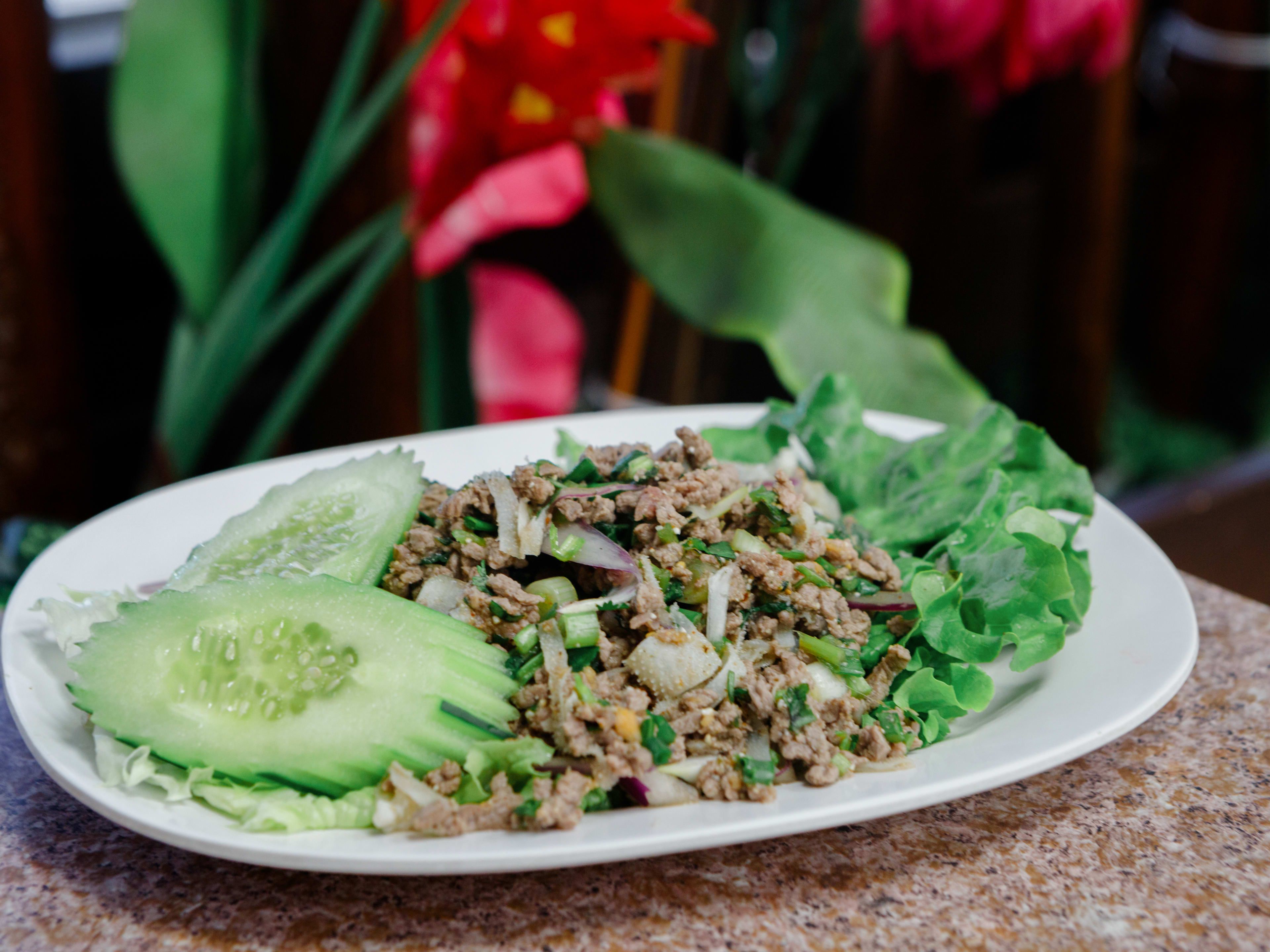 plate of thai beef lab salad with cucumber rounds in front of pink flowers