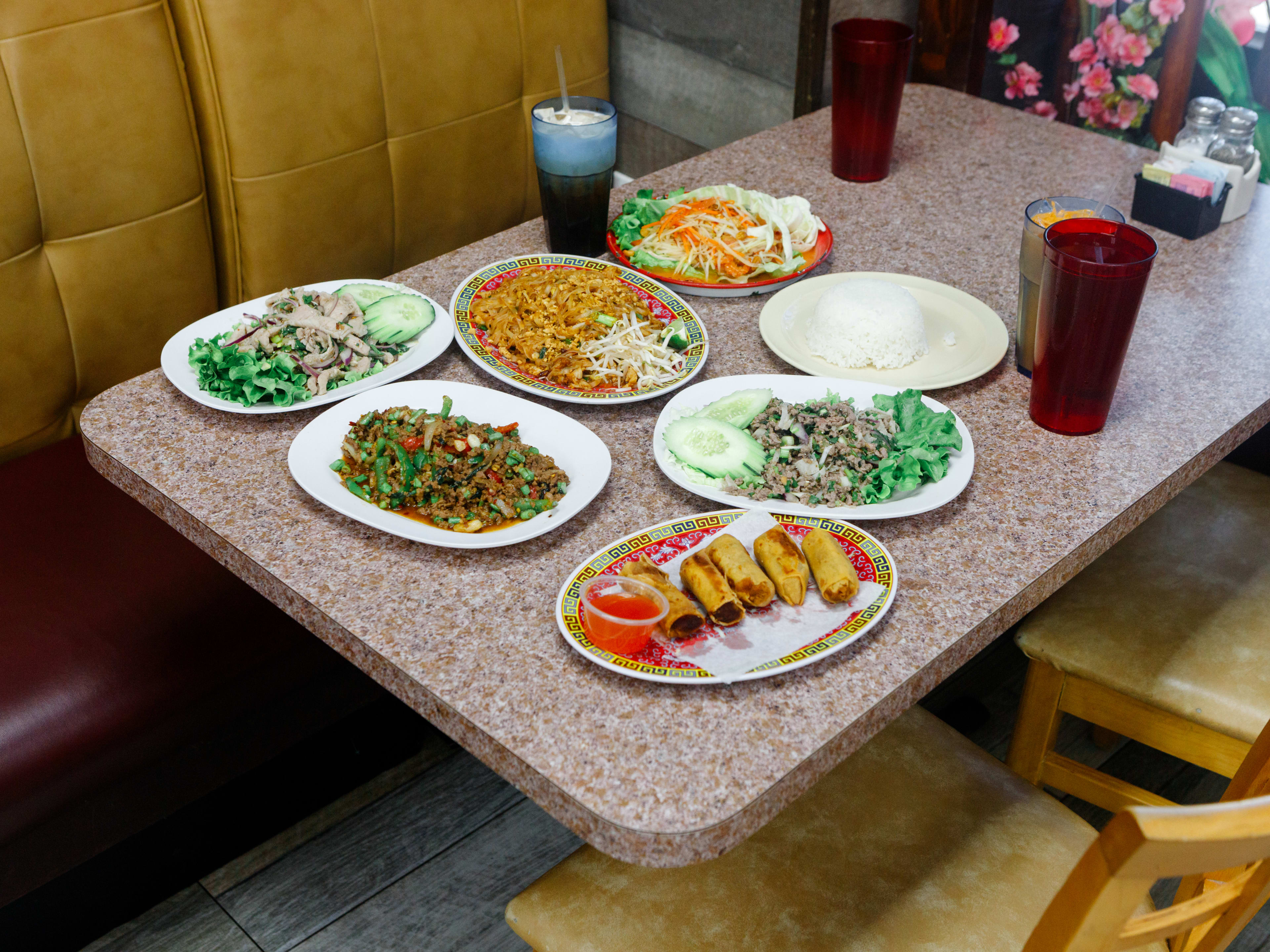 spread of thai food dishes and drinks on a linoleum booth table