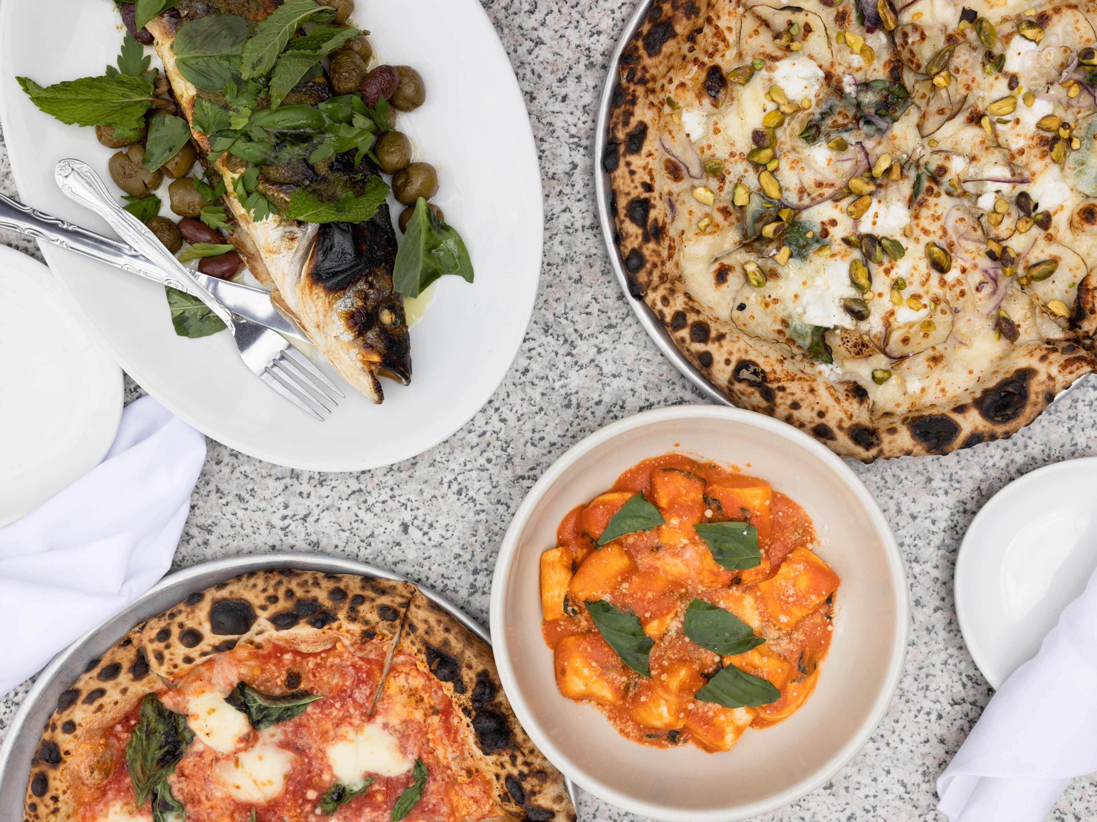 A food spread with pizzas and pasta bowls.