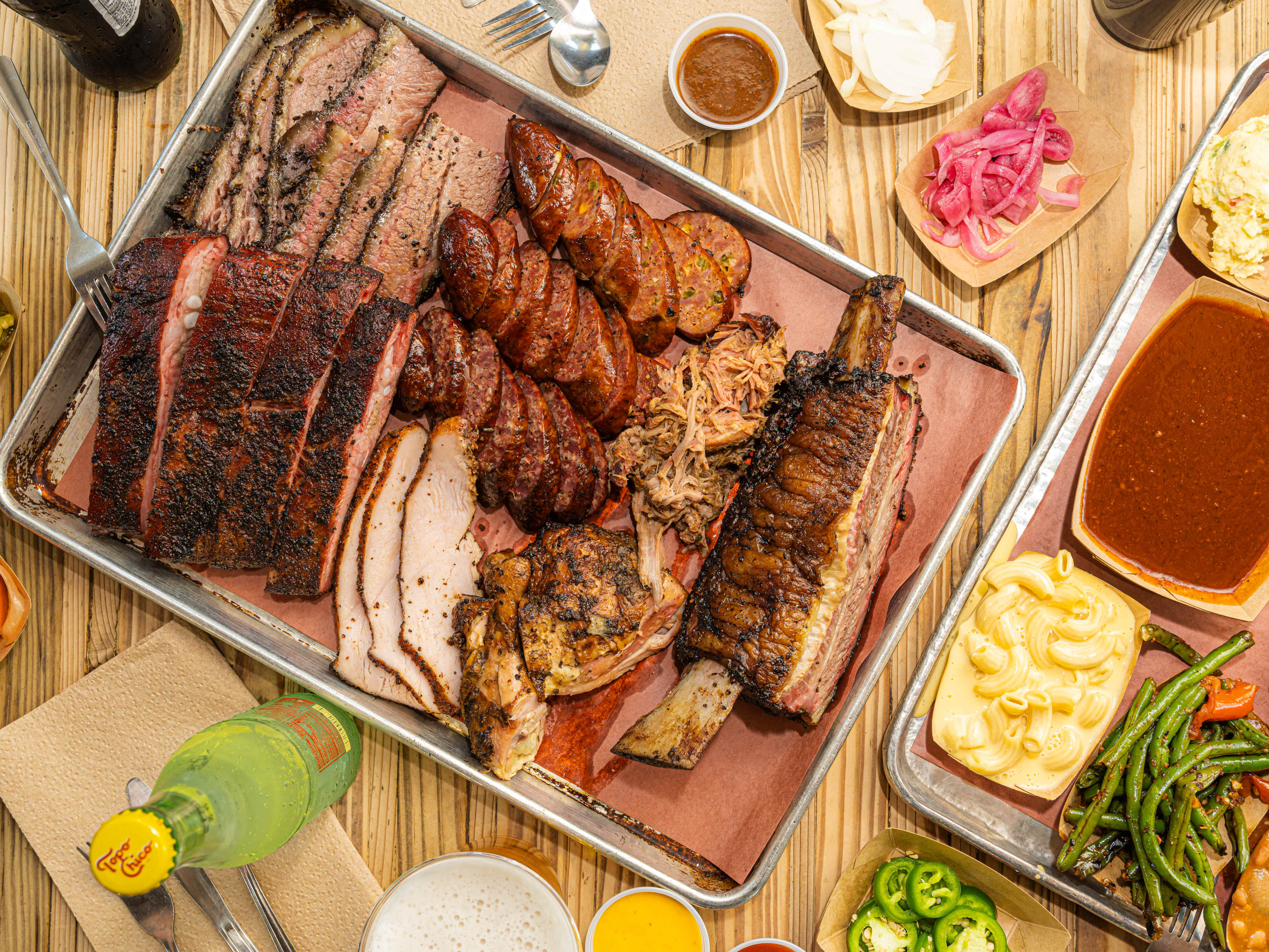 A bbq platter from The Pit Room surrounded by sides and drinks.