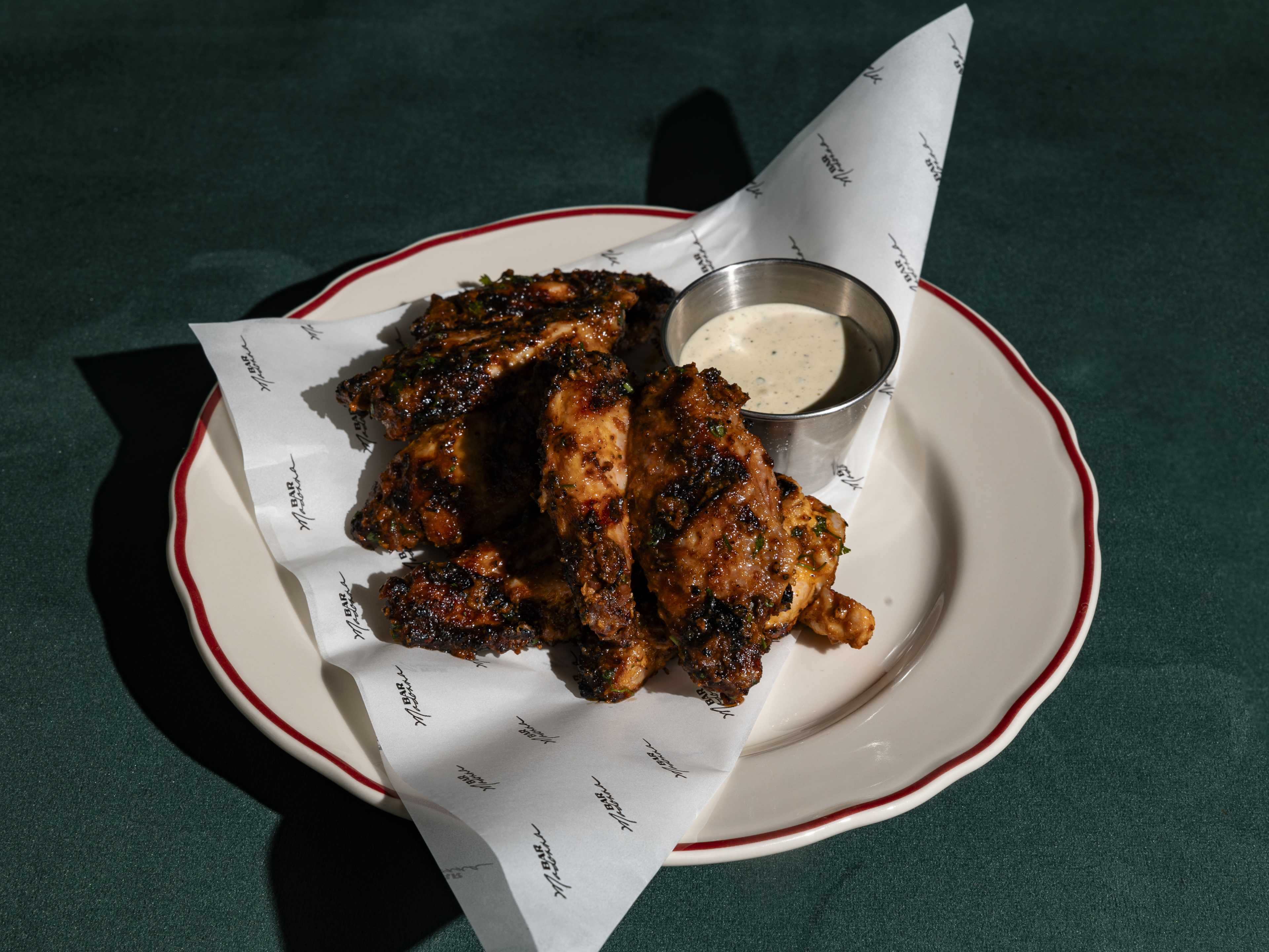 A plate of charred wings with a sauce on the side.