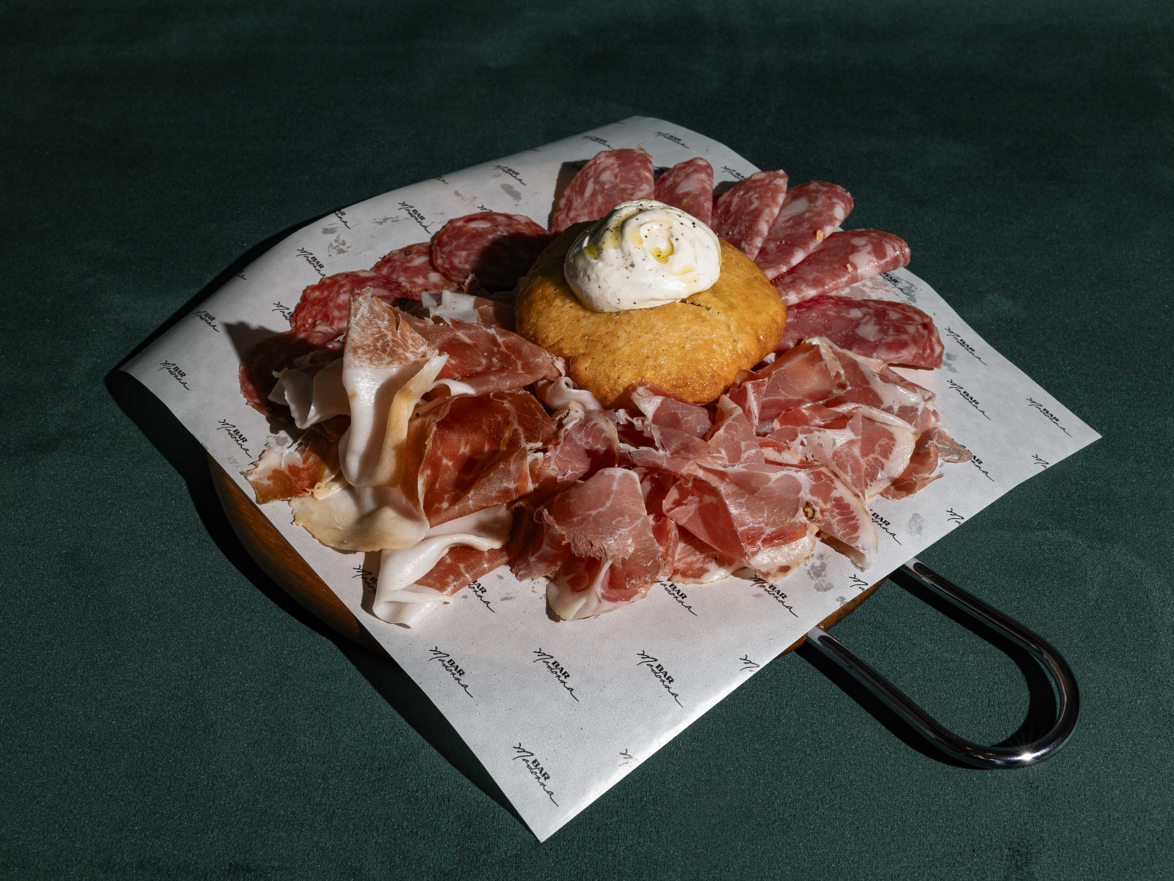 A big board covered with charcuterie, with a piece of fried bread in the middle.