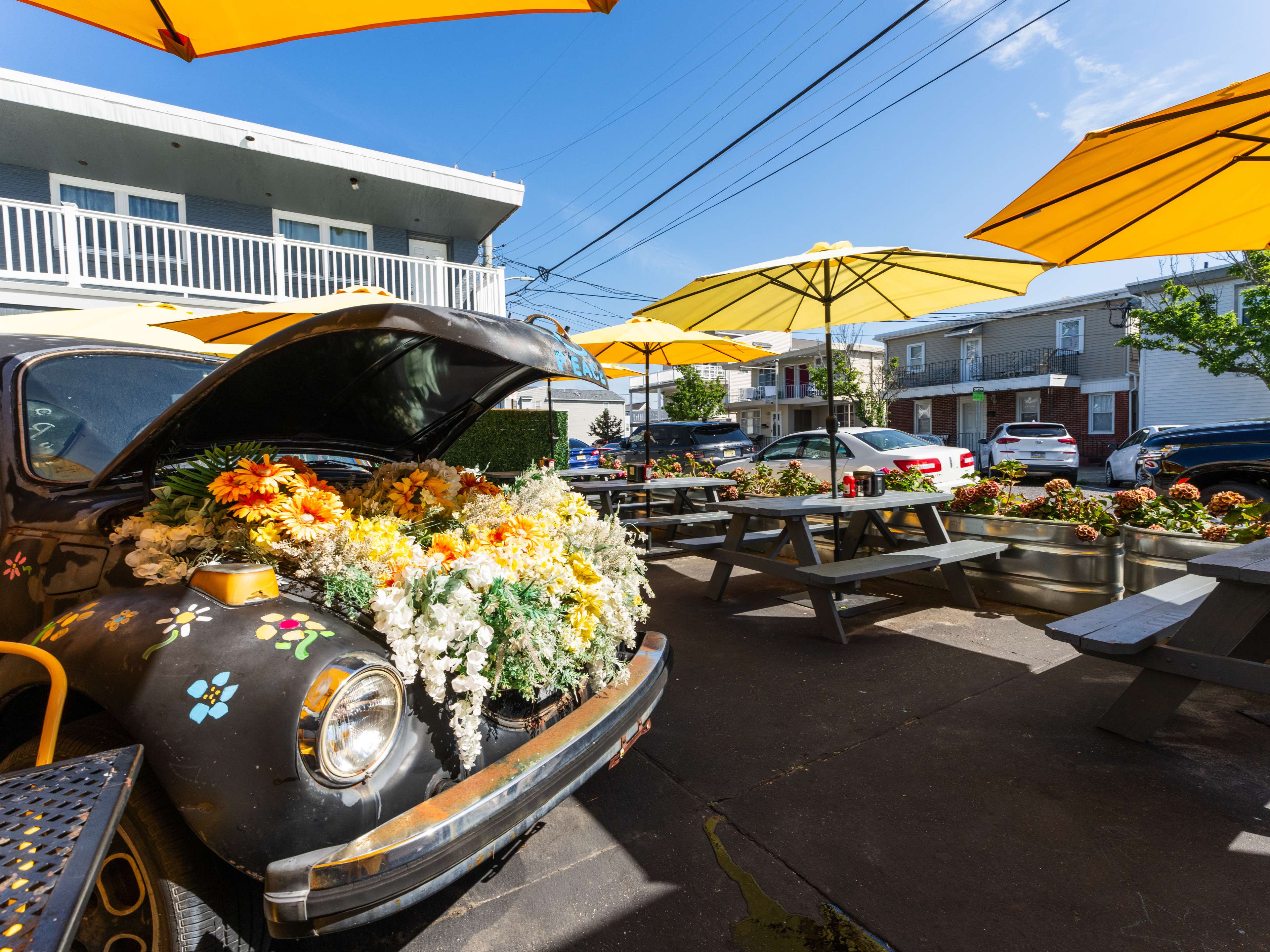 exterior of bagel shop with picnic tables and colorful umbrellas and an old car with fake flowers in the hood