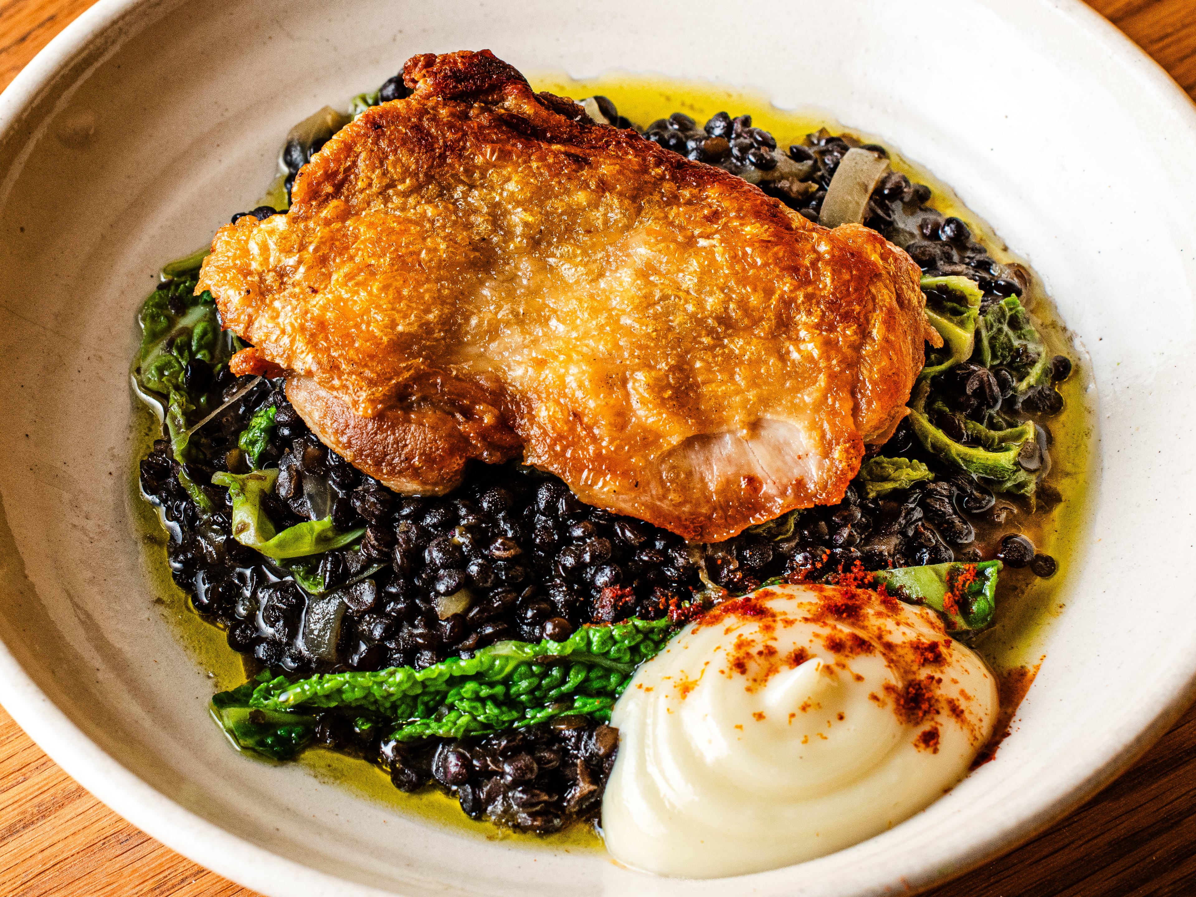 Beer braised chicken thigh with lentils, onions, garlicy aioli, and savoy cabbage, served in an off-white bowl.