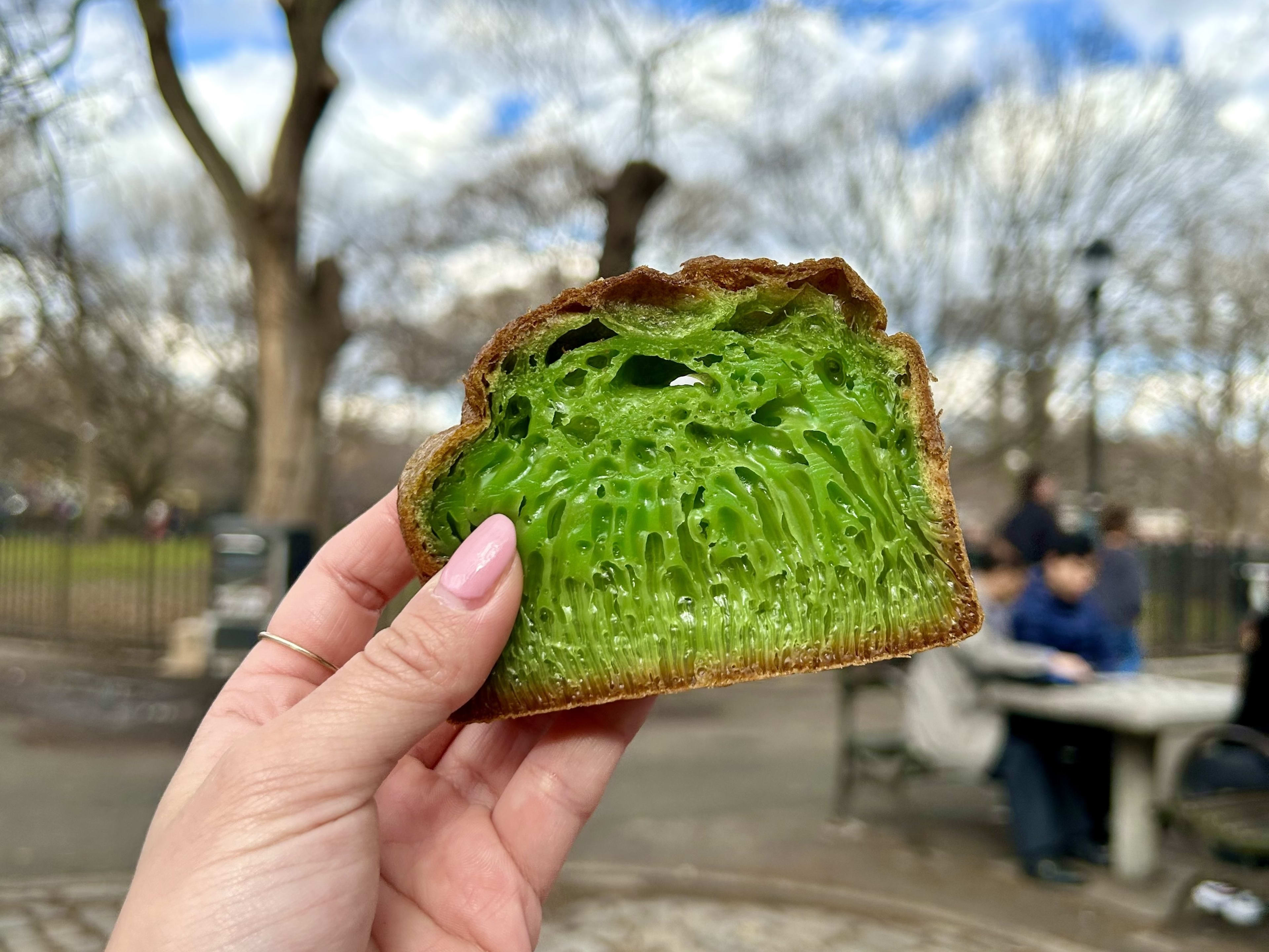 A slice of bright green cake being held in a park.