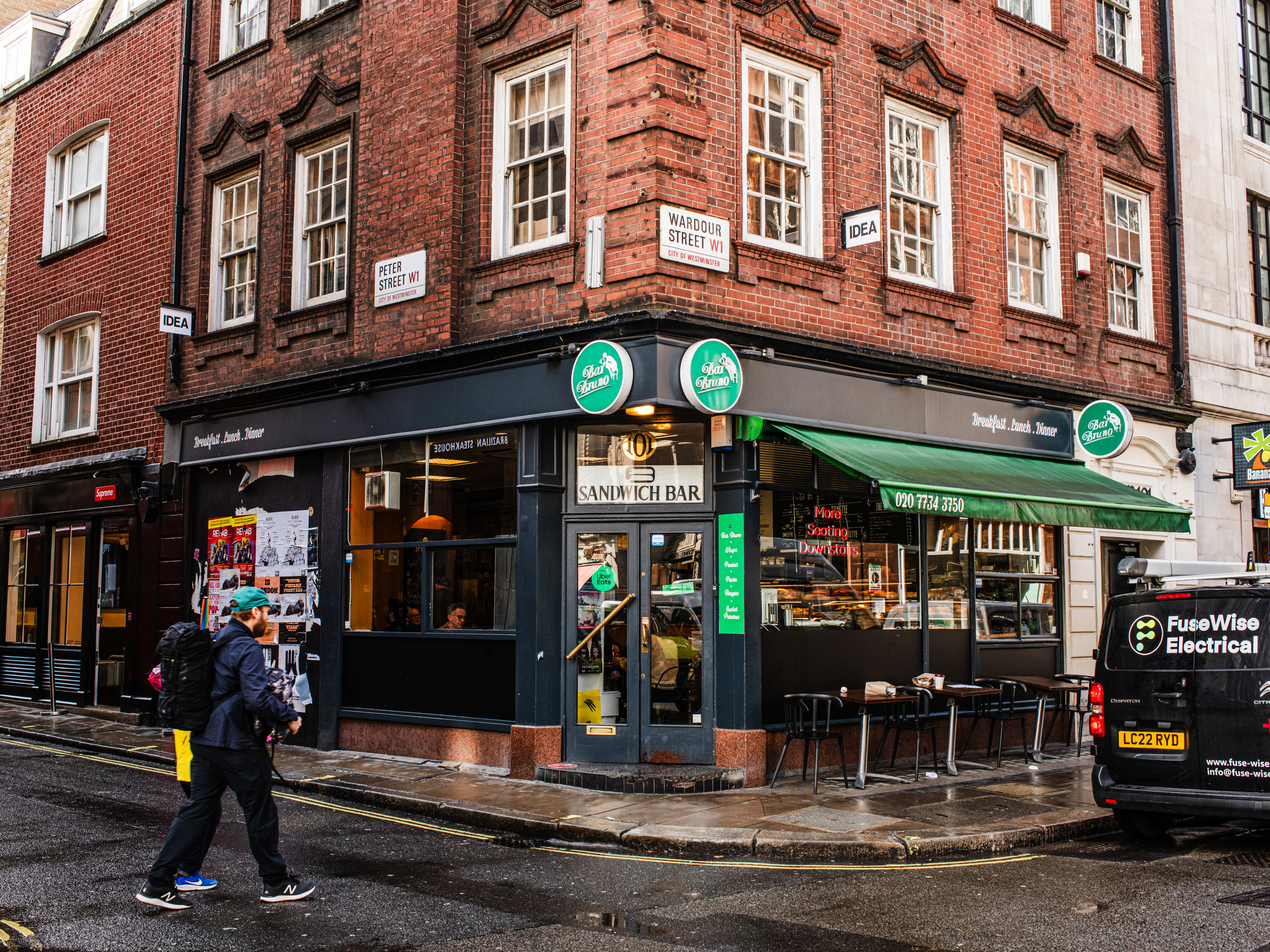 The exterior of Bar Bruno. It is on a corner, there are small tables for dining outside, and a green awning.