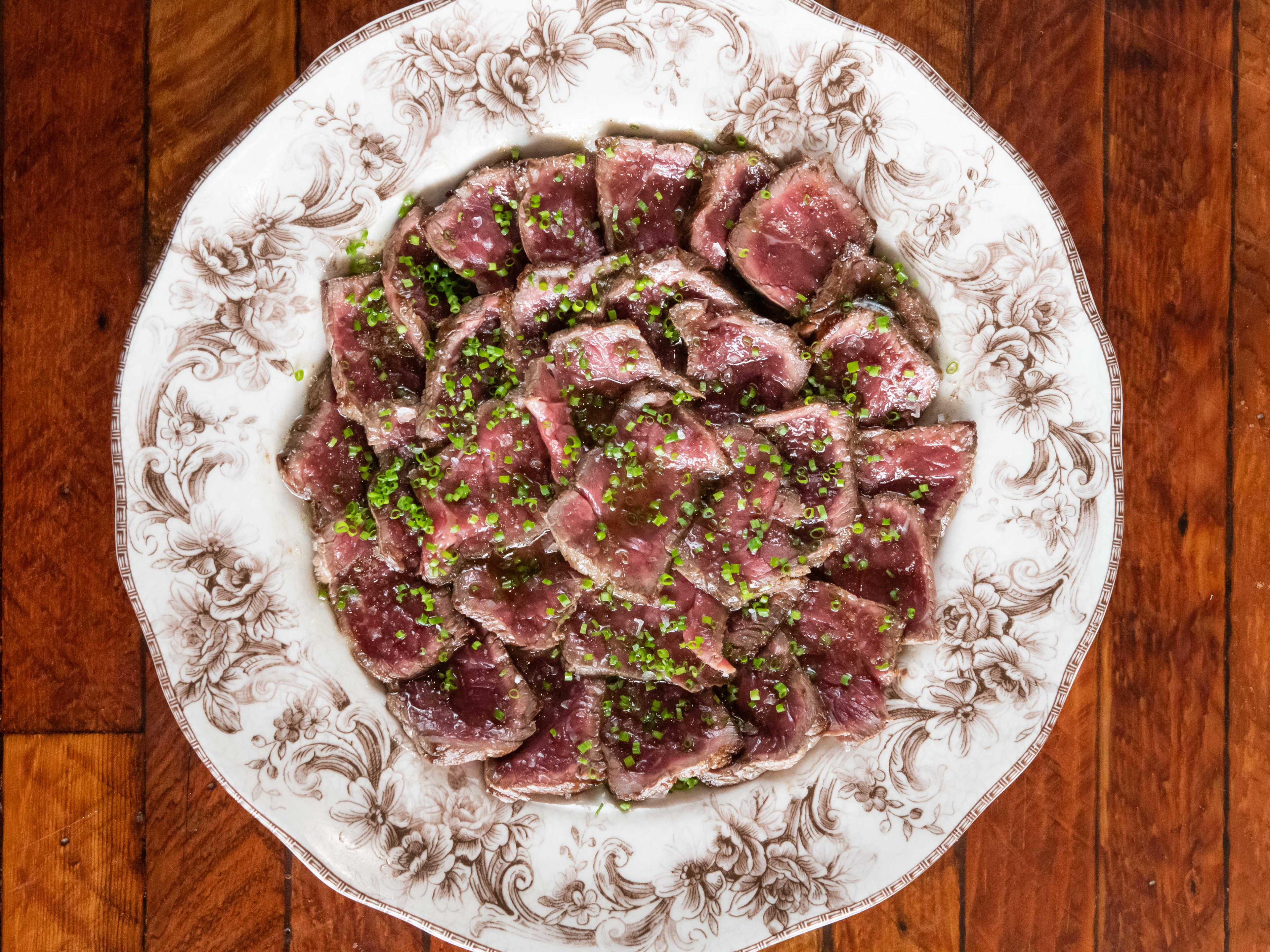 plate of rare steak slices topped with chives