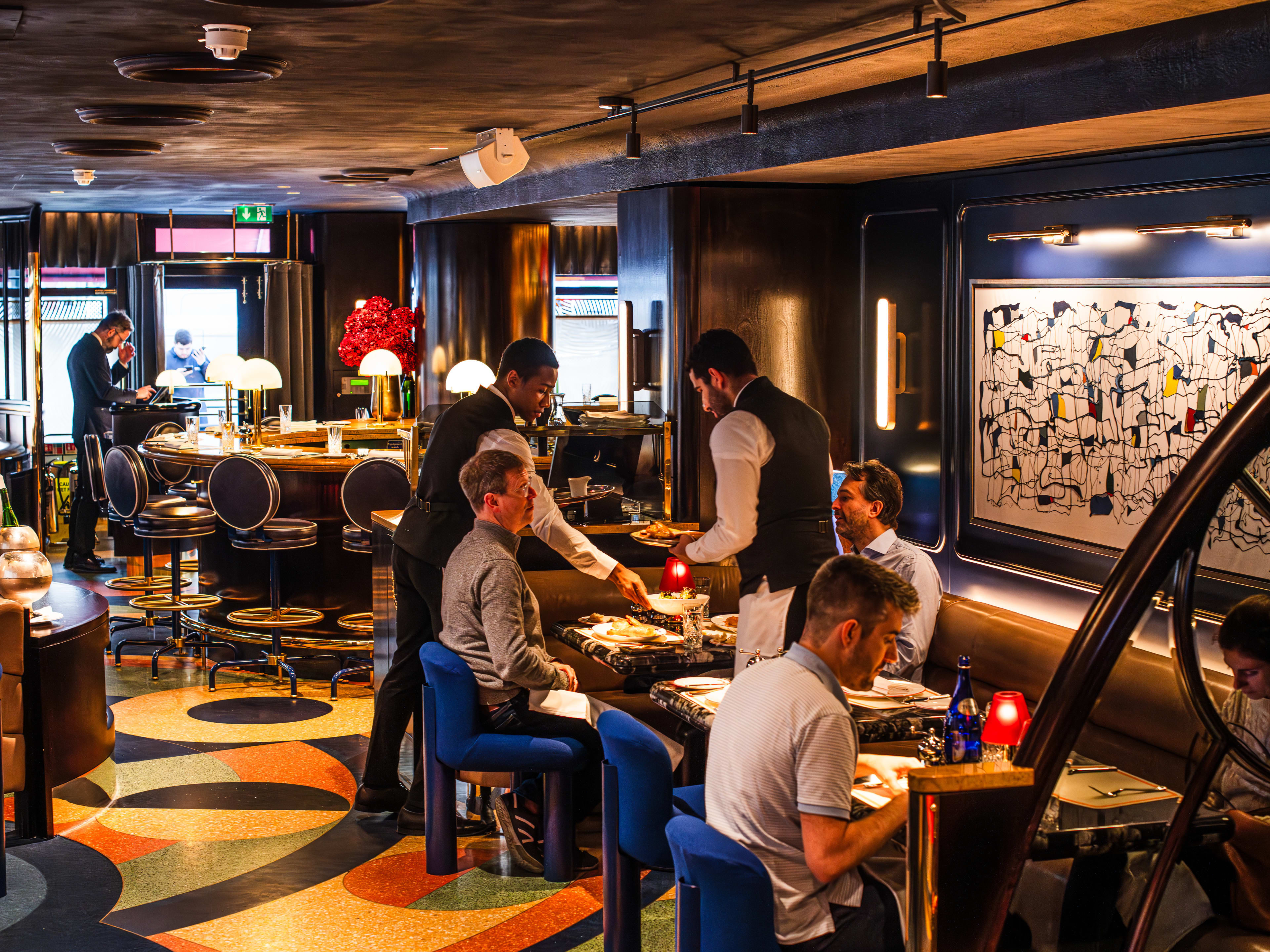 The colorful and patterned interior of Bebe Bob with patrons at tables sitting in leather booths and blue mod chairs.