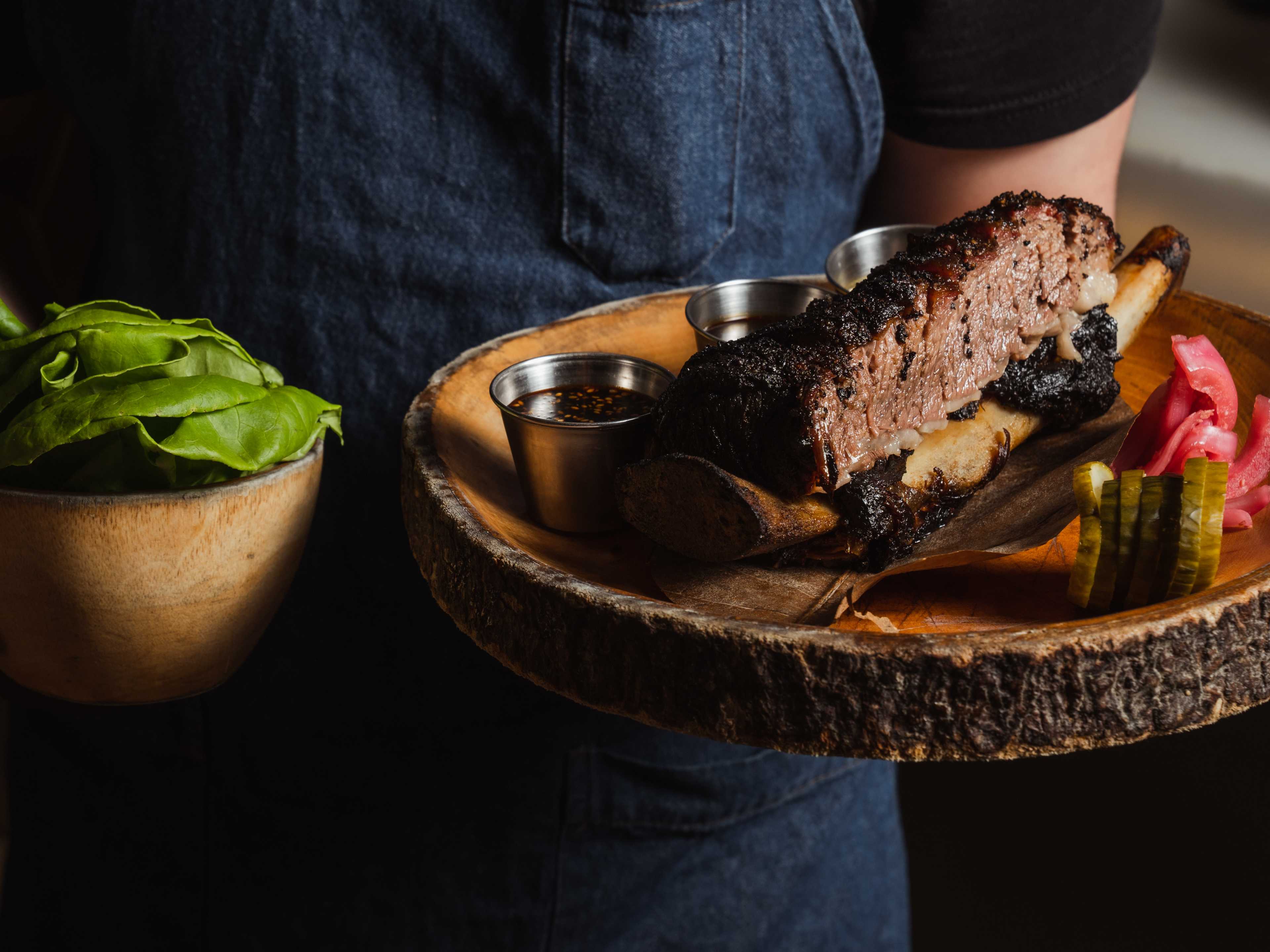 Beef short rib on a wooden plate with a side of bib lettuce and an assortment of sauces