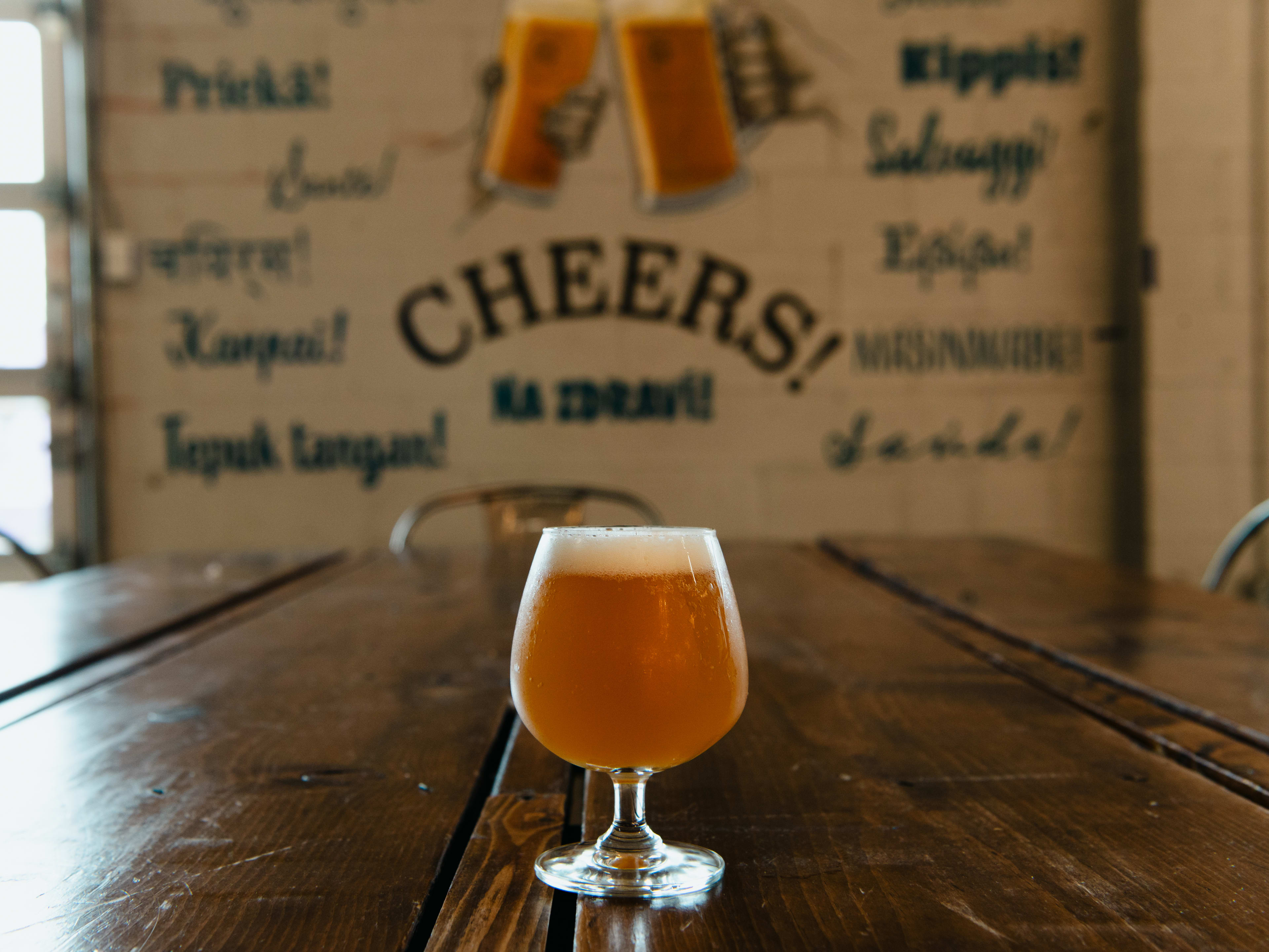 A beer sits in front of a "cheers!" sign.