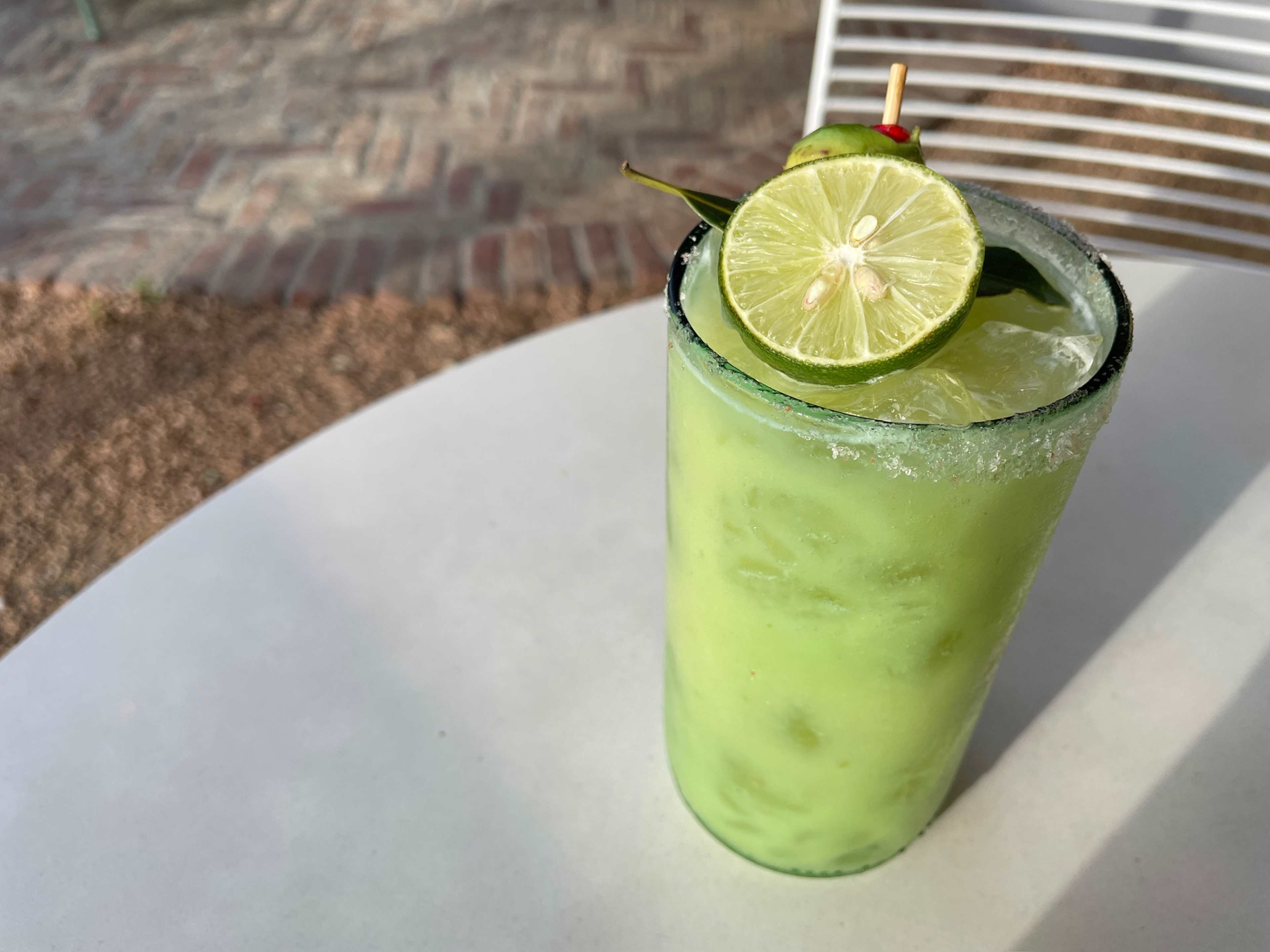 creamy green liquid in a tall glass with a small lime wedge on a white table