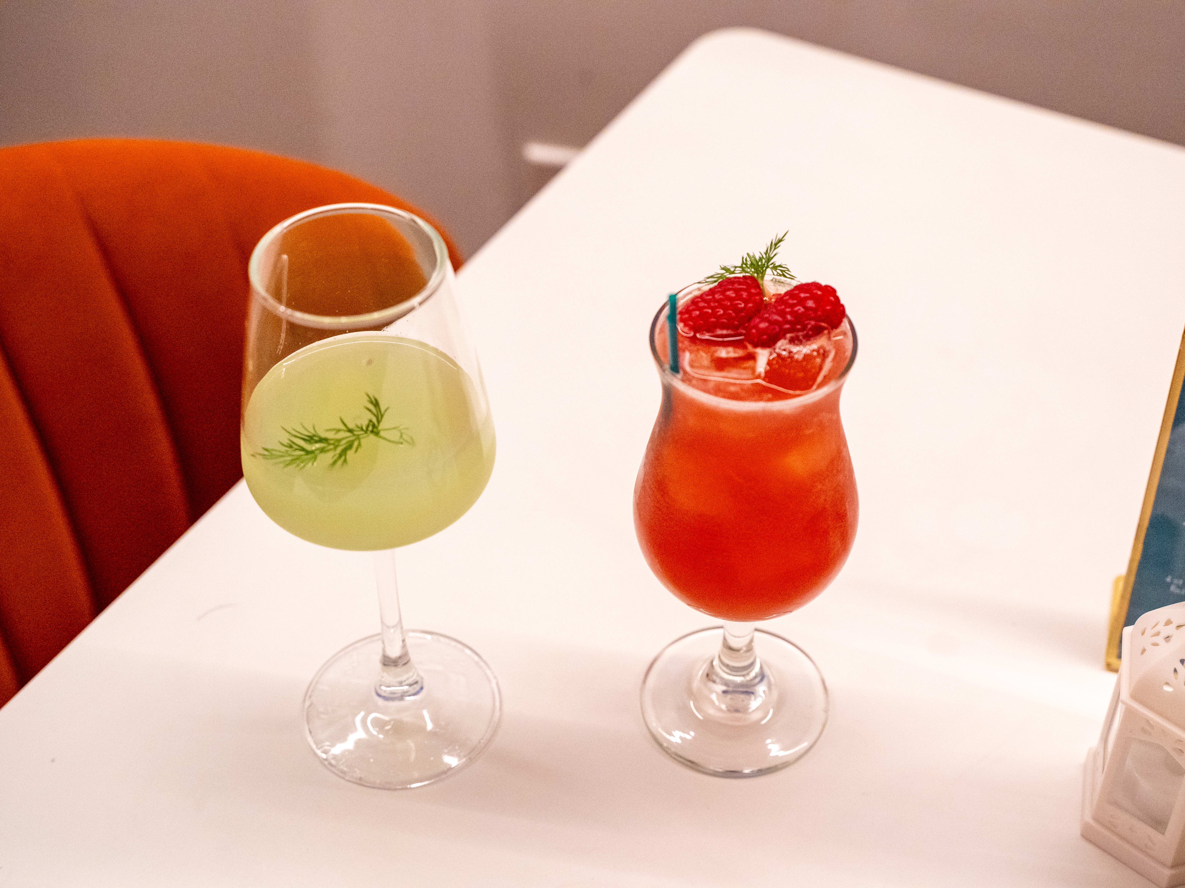 Two drinks with fruit and herb garnishes on a table