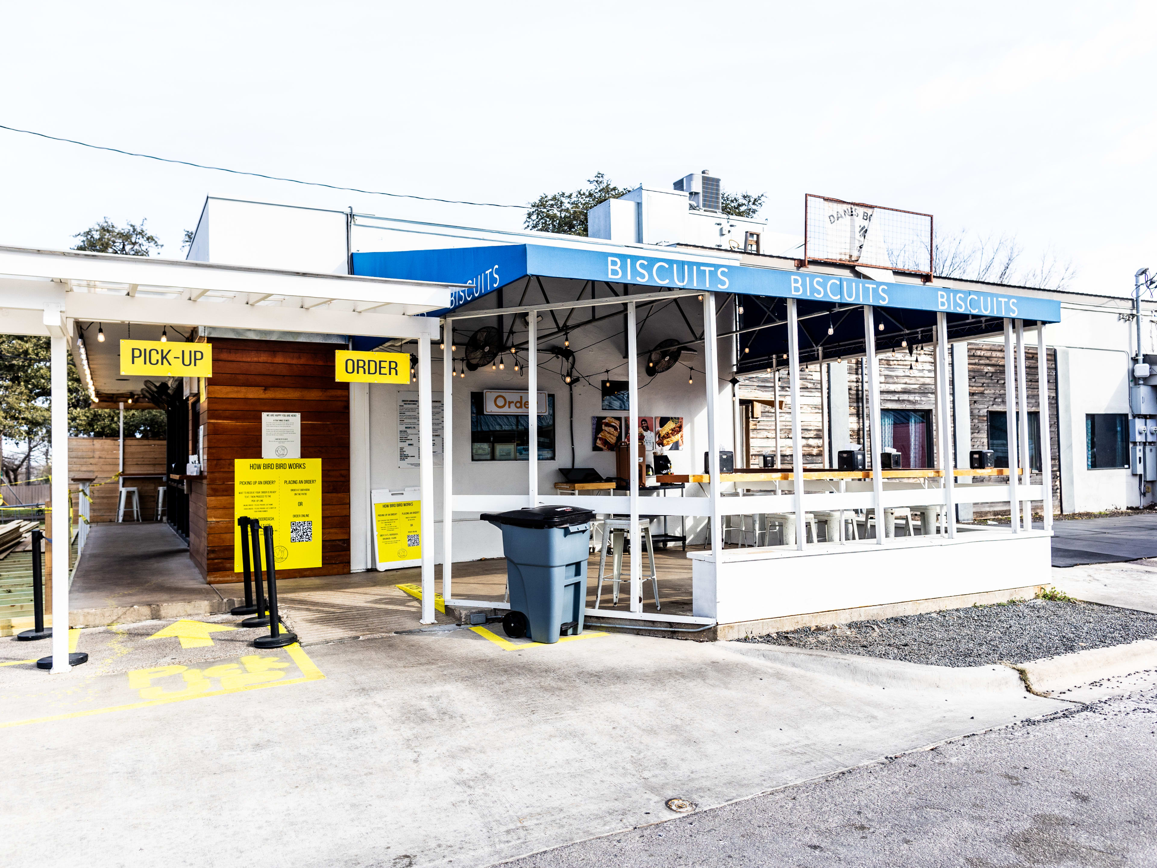 The exterior of Bird Bird Biscuit with a small patio eating area and yellow signs for where to order and pick up.