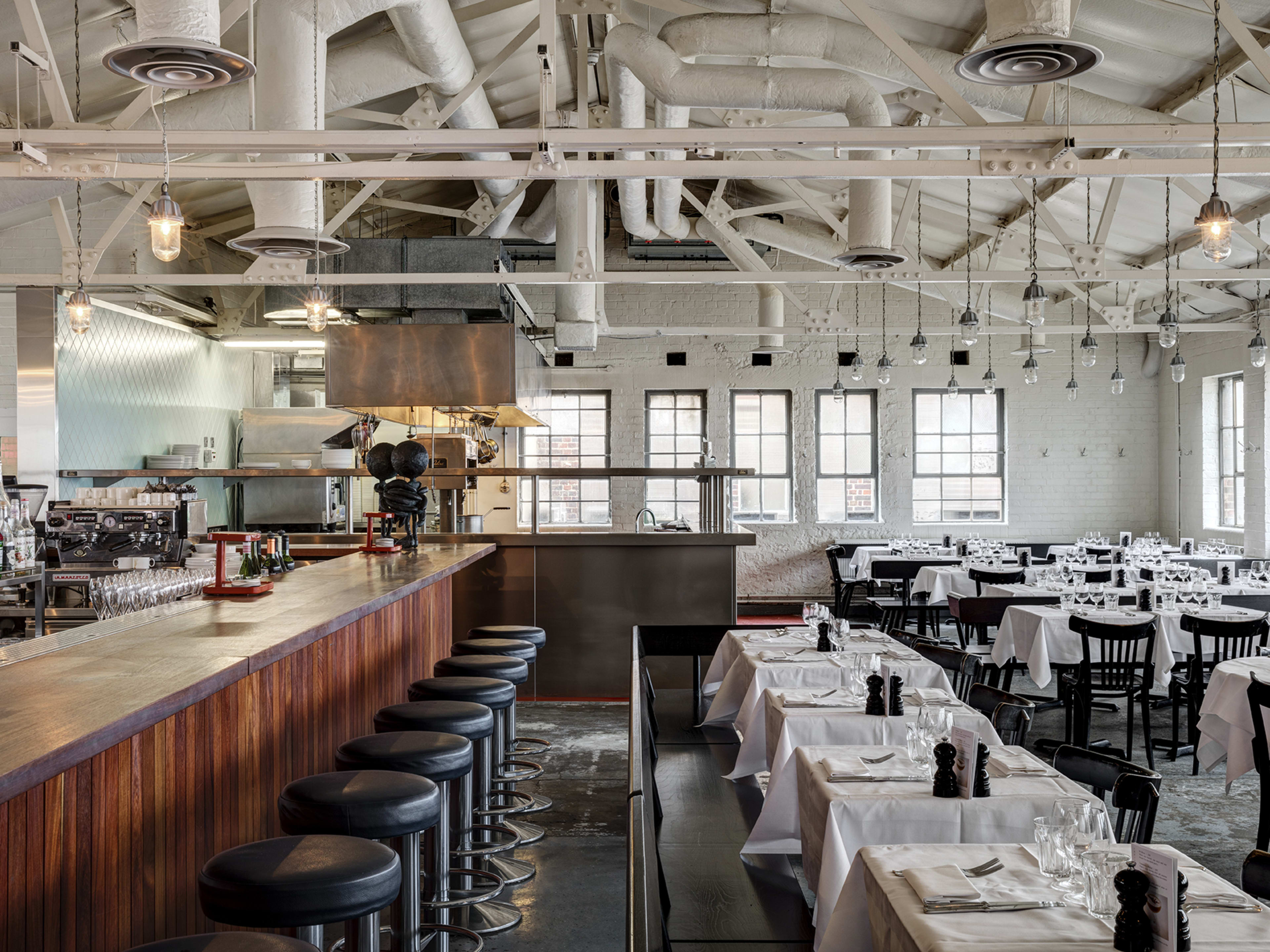 The industrial white interior of Bistrotheque. There is a bar and tables with white tablecloths.