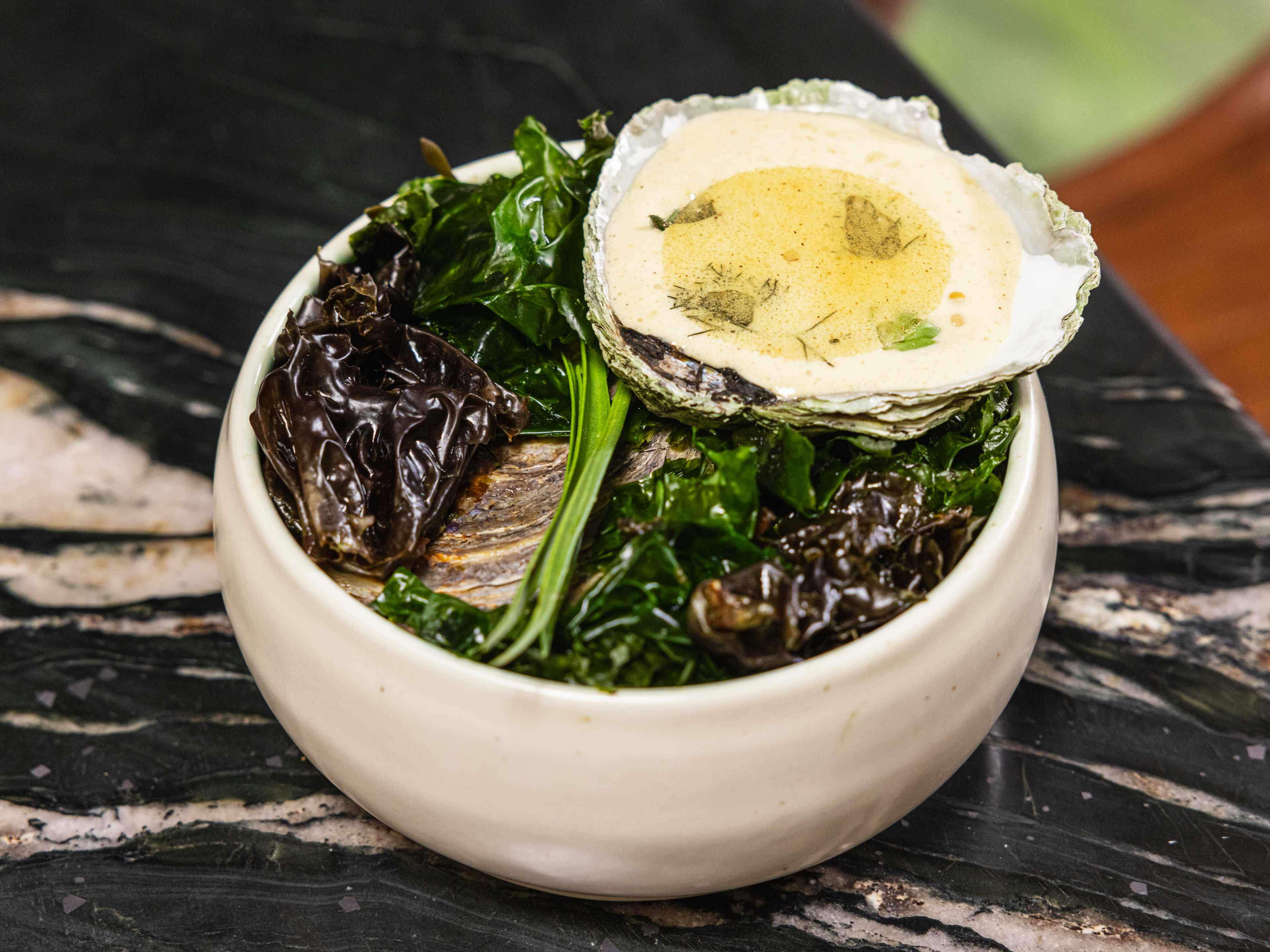 A belon oyster on top of kelp in a white ceramic bowl.