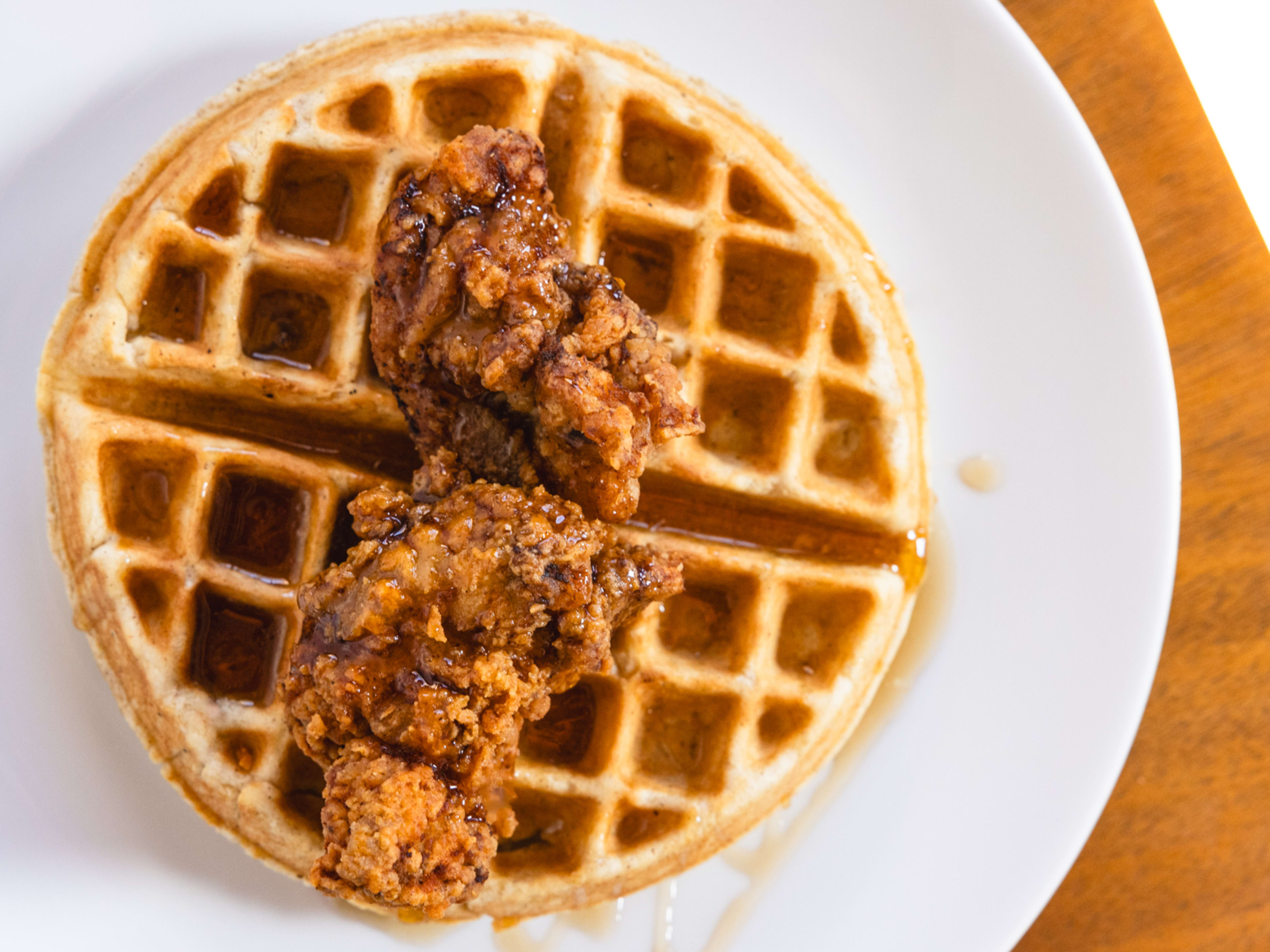 Waffle on plate topped with a fried chicken tender and drizzled with syrup.