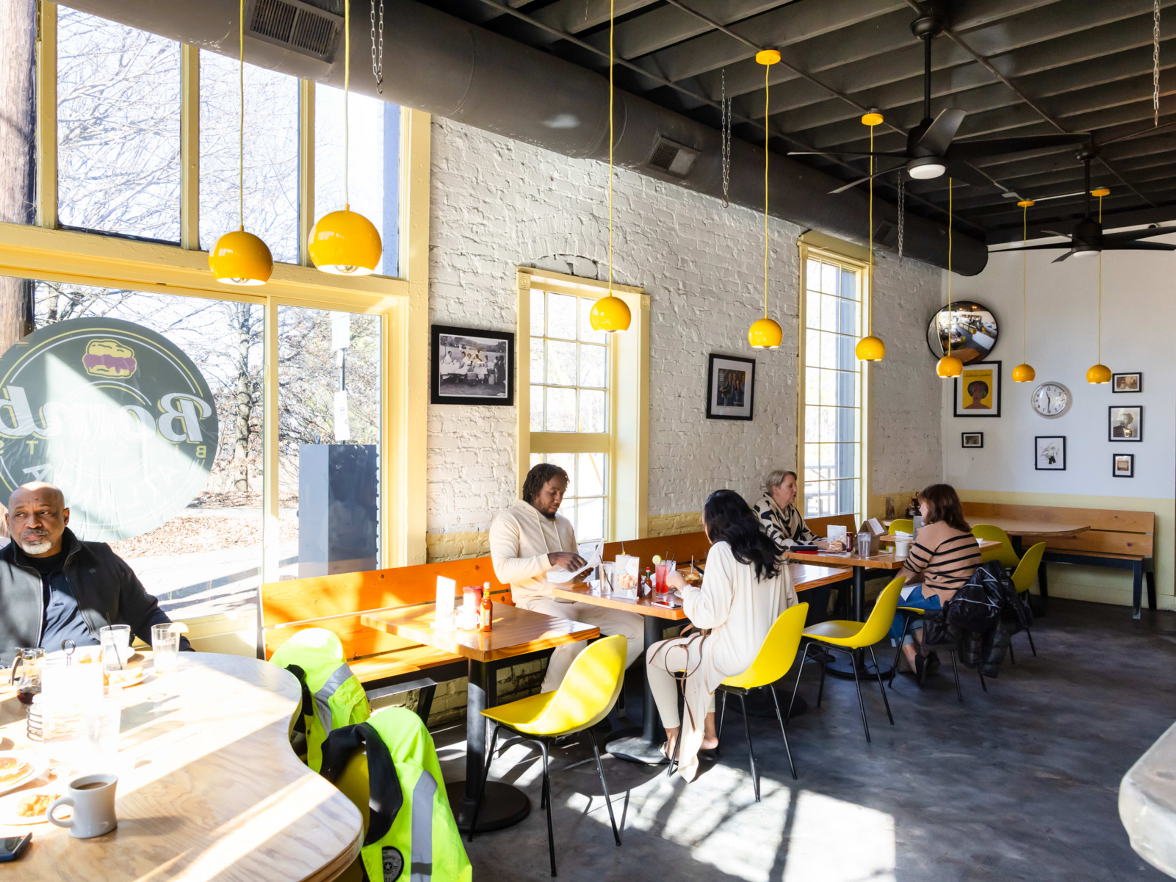 bright interior with yellow hanging lights, big windows, and folks sitting in wooden booths at tables