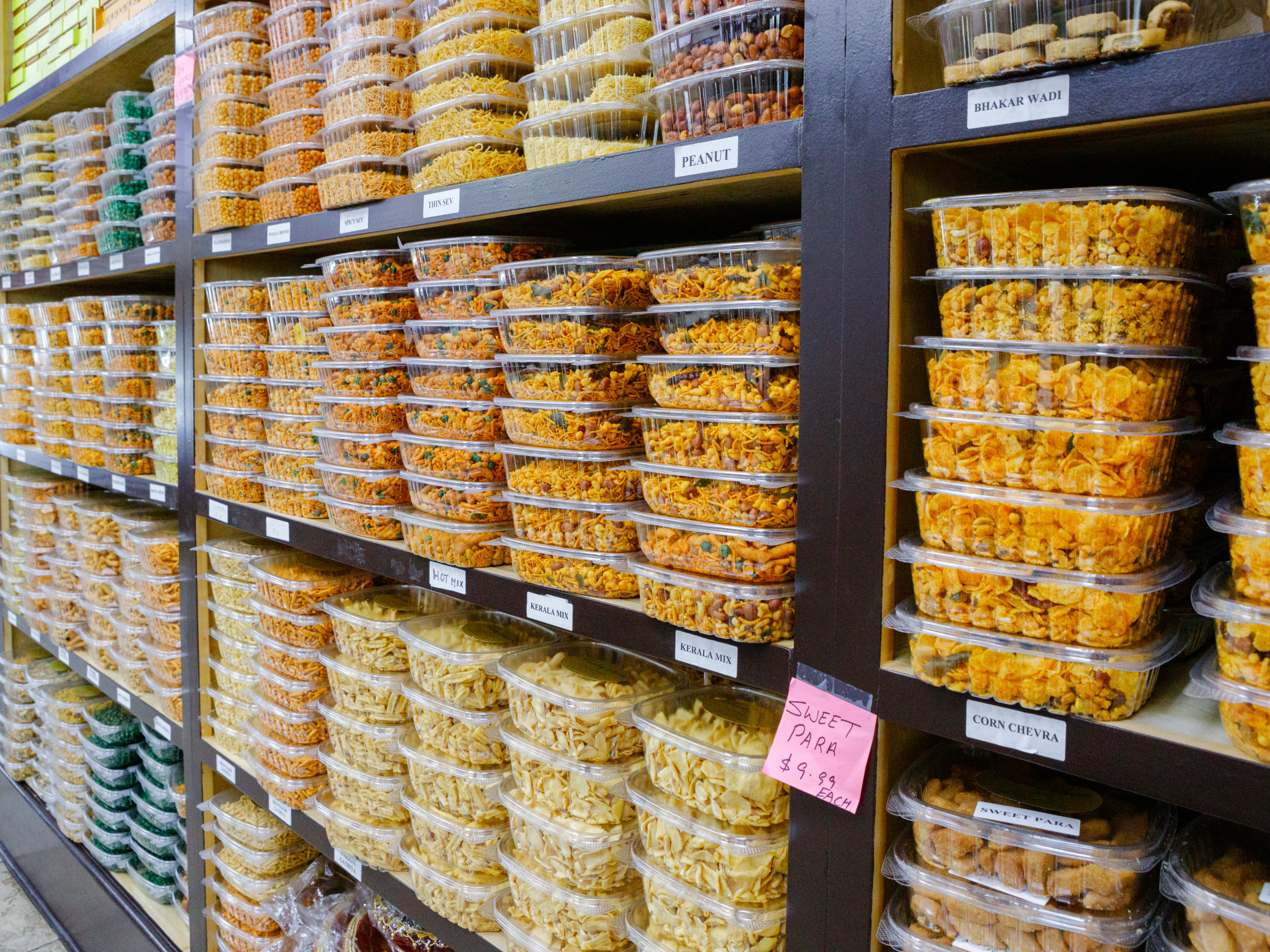 snack mixes in plastic containers on shelves at Bombay Sweets.