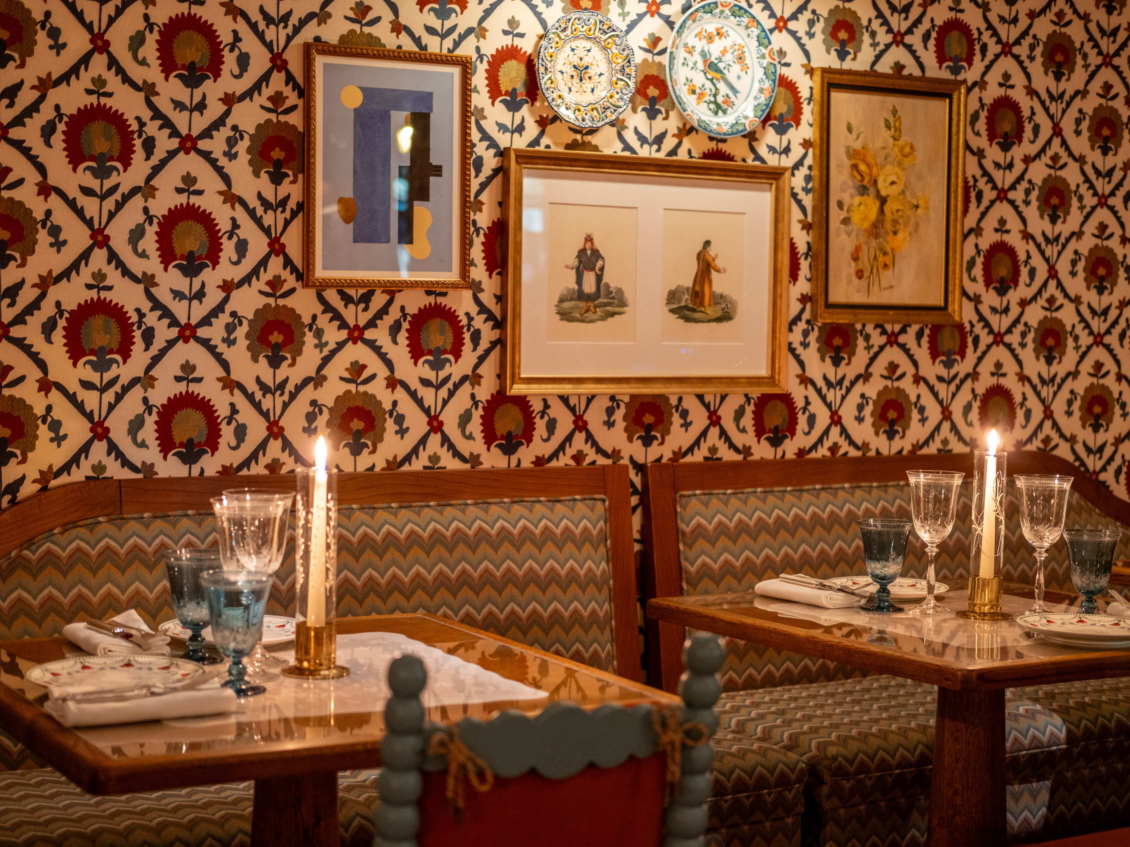 Tables in front of a wallpaper wall with framed art and candles at Boubale in Paris