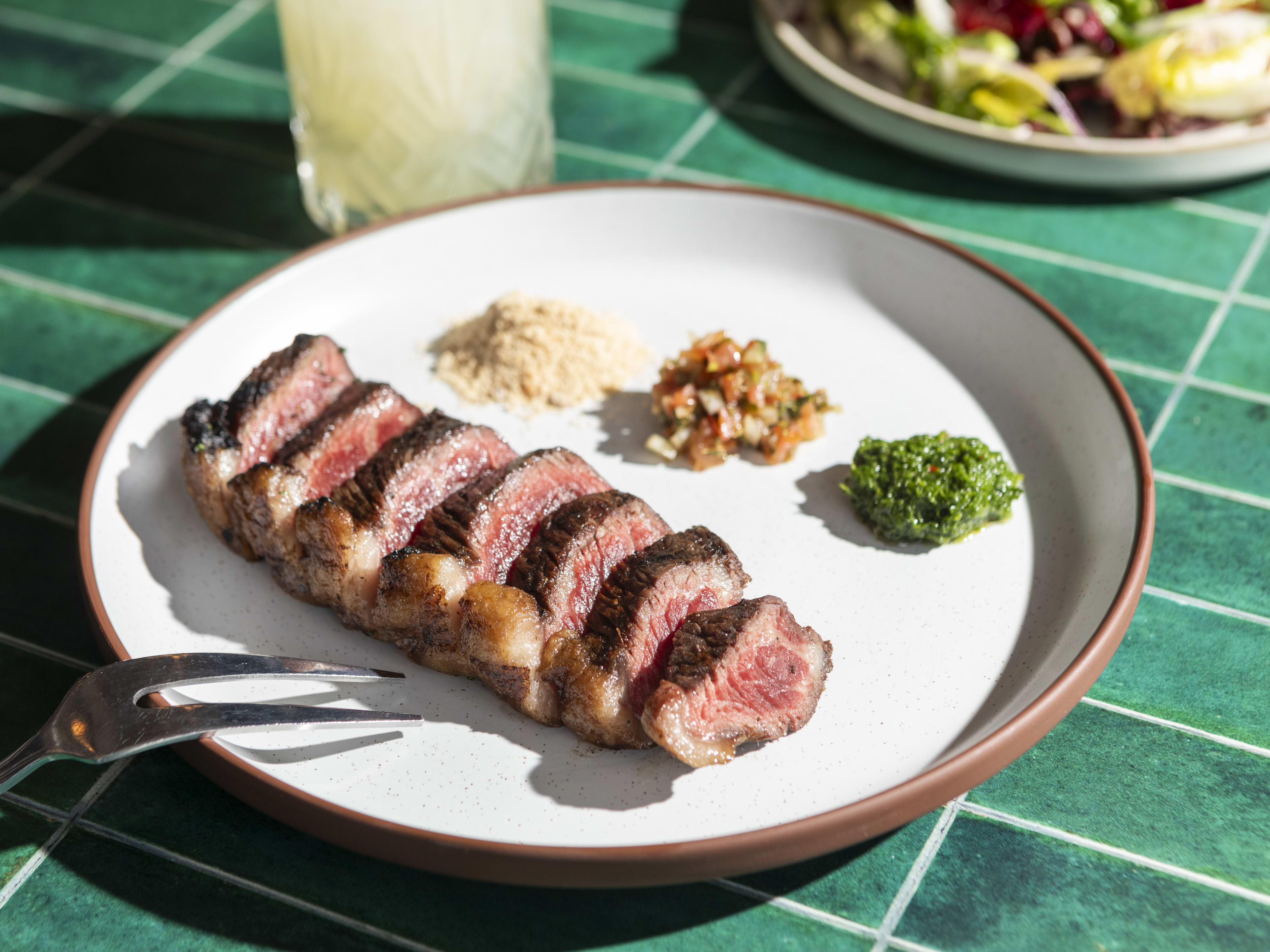 Plate of sliced prime rib steak with three salsas lined up next to it