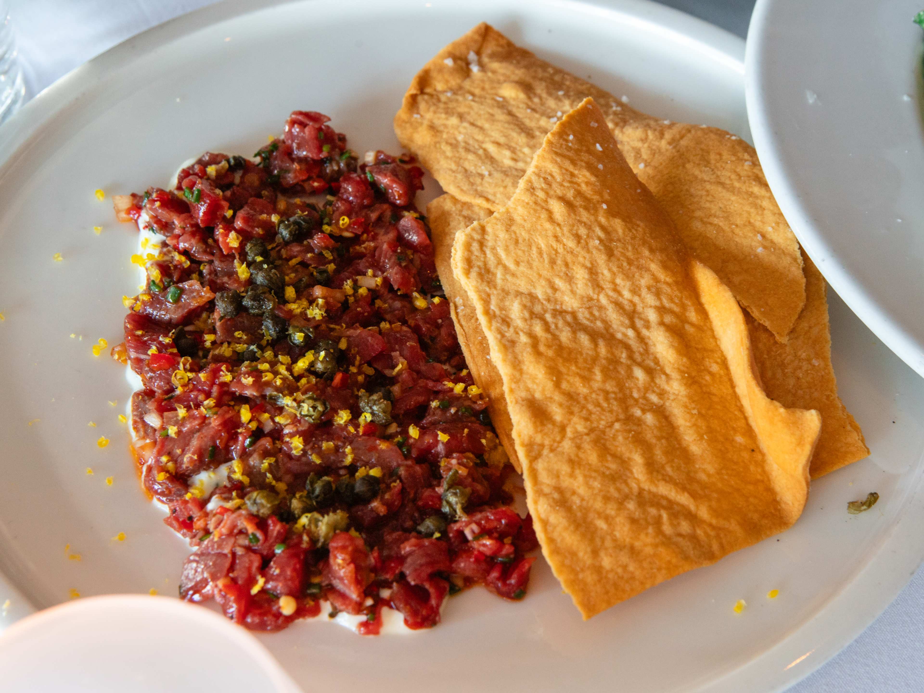 plate of minced tartare topped in shaved egg yolk with a pile of lavash chips