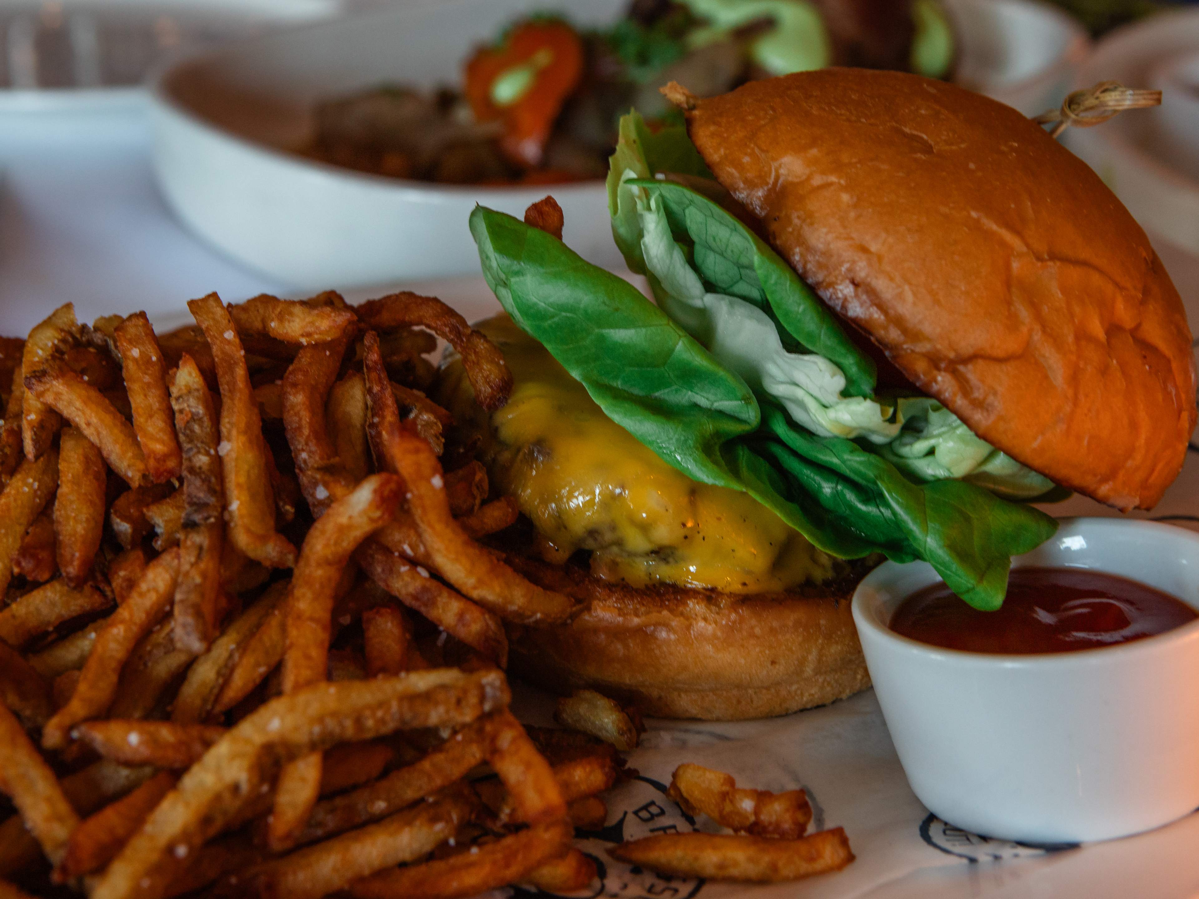 cheeseburger with a brioche bun and lots of bibb lettuce next to a pile of crispy fries