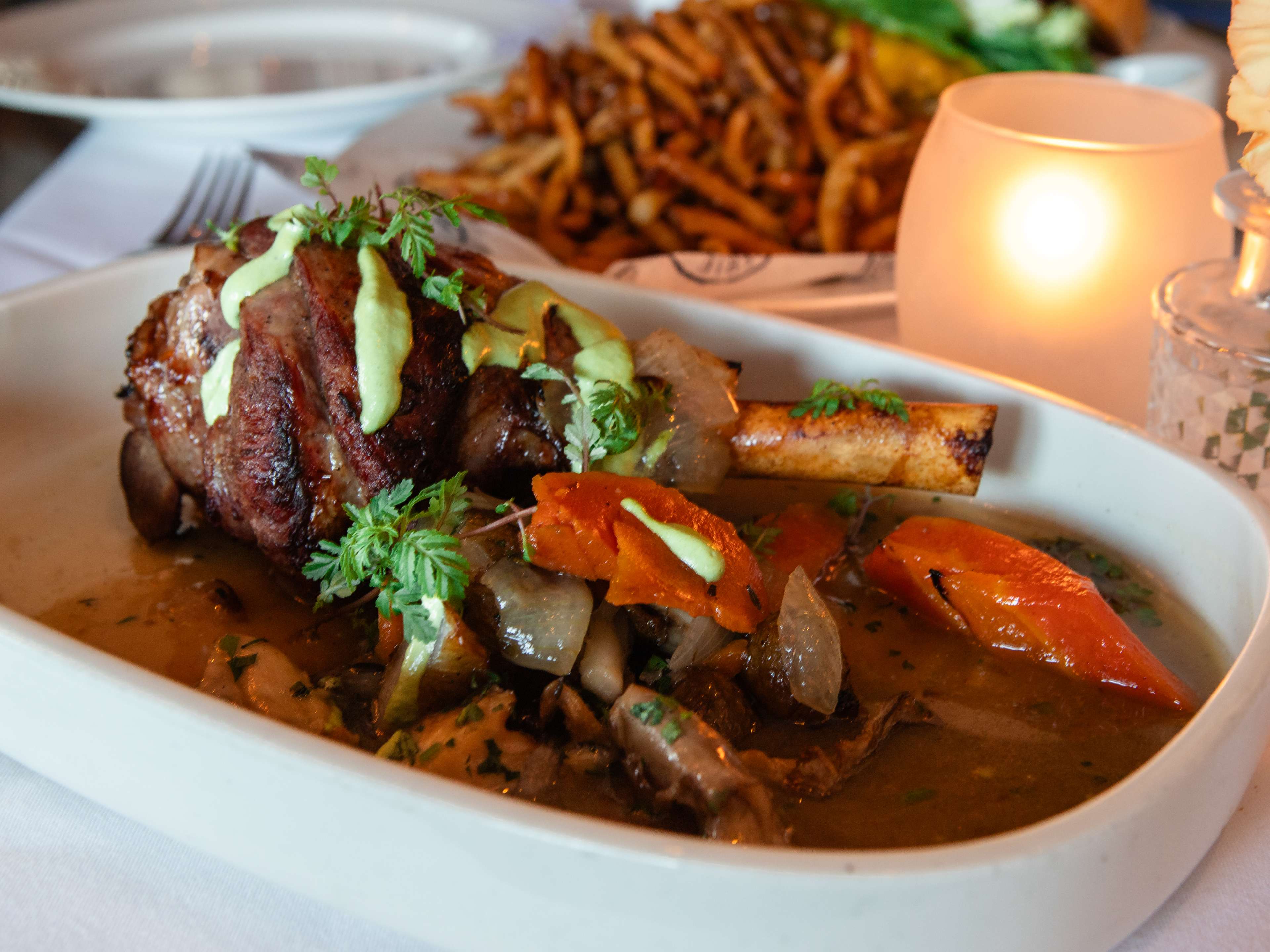 large roasted leg of lamb surrounded by roast carrots and topped with a drizzle of green sauce