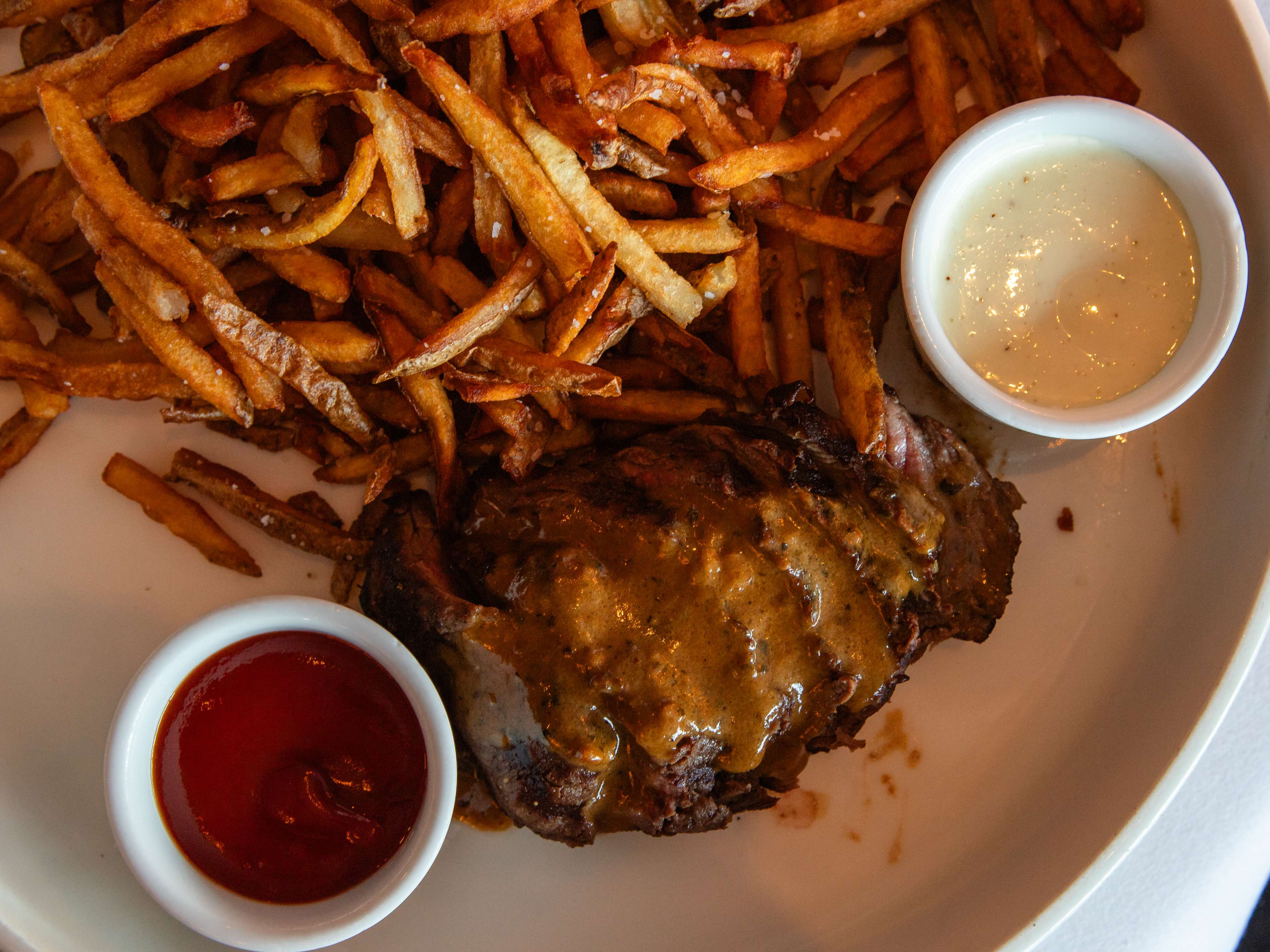sliced beef filet covered in au poivre next to ramekins of mayonnaise, ketchup, and a mound of crispy french fries