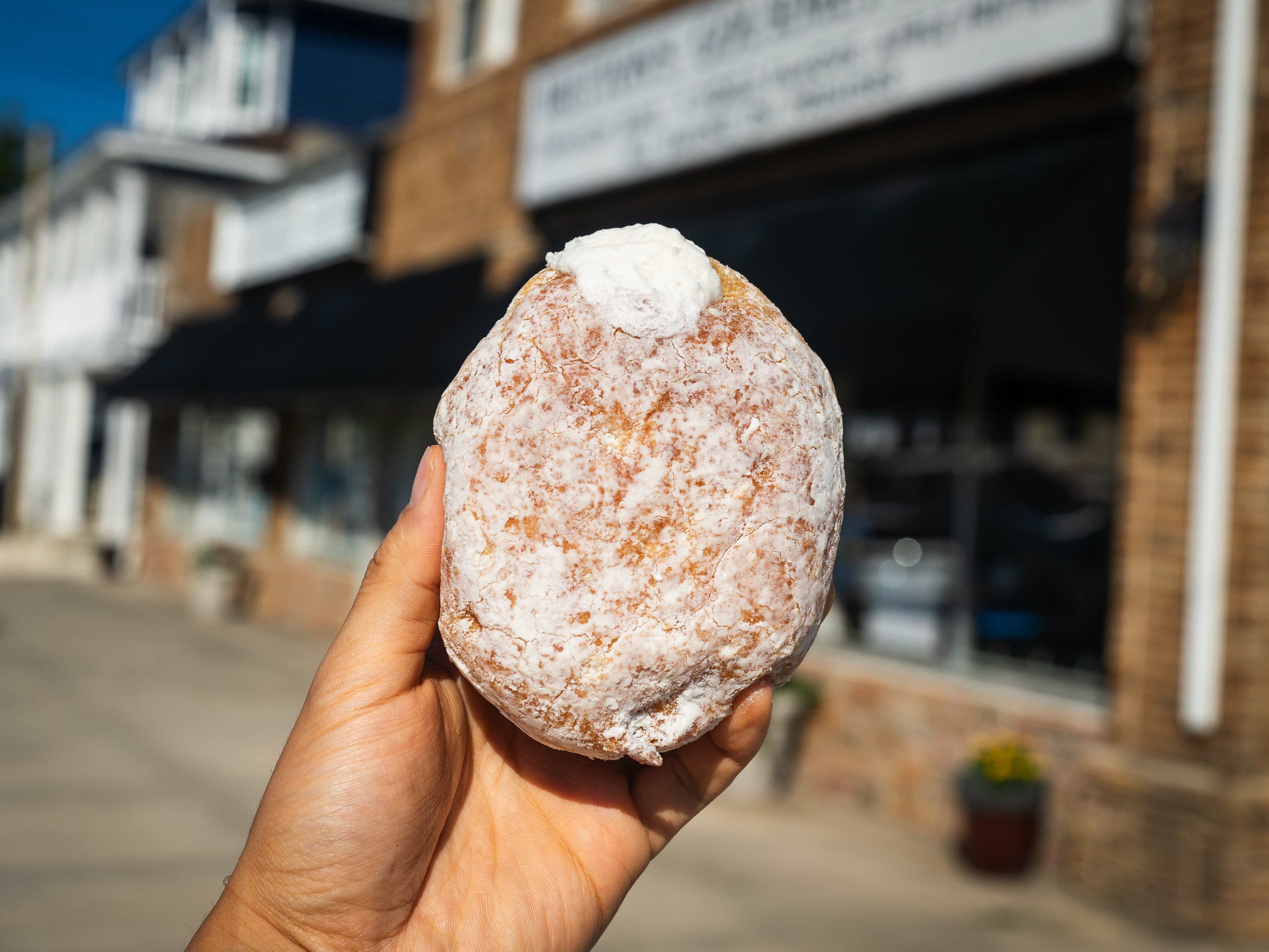 Hand holding a Mega Cream Donut outside of donut shop.